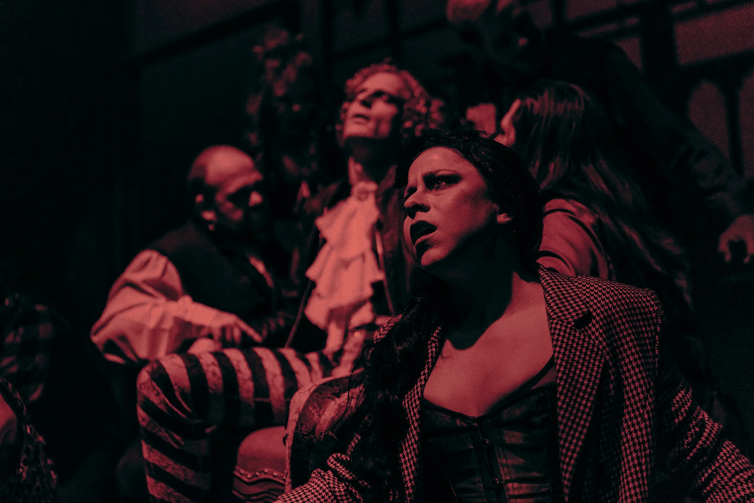 Dramatic scene with people in expressive poses under red lighting, wearing vintage-style costumes.