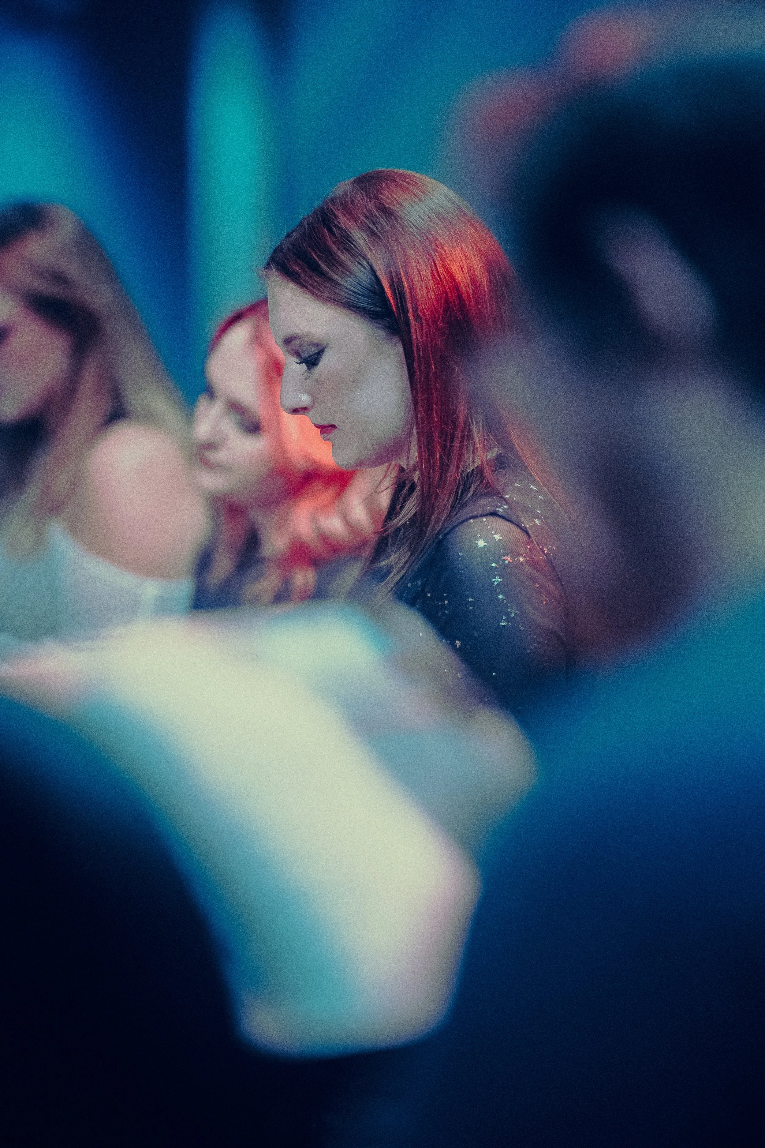 People in a dimly lit setting, focusing on a woman with red hair, soft focus, nightclub or party atmosphere.