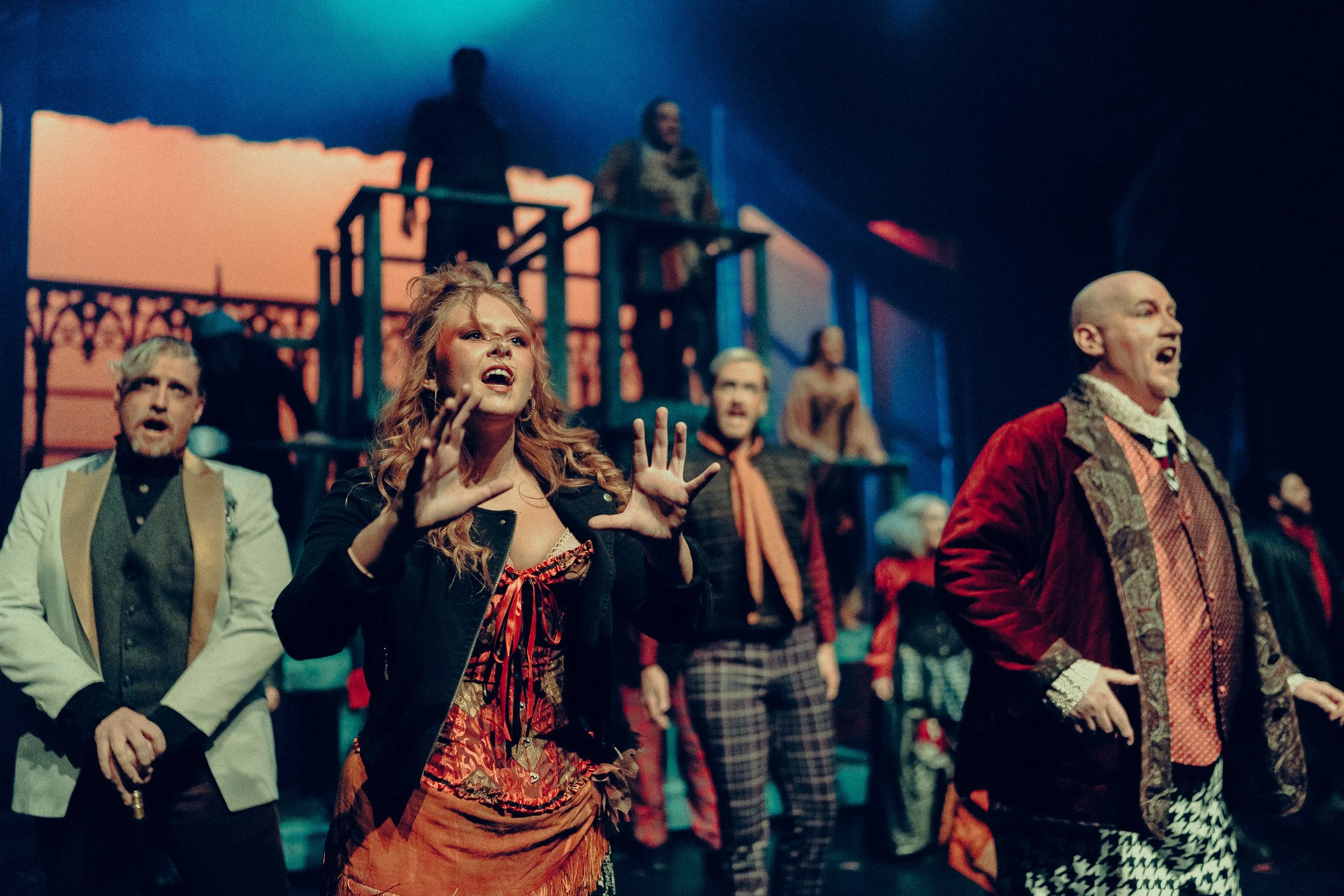 Stage performance with actors in period costumes singing passionately, set with dramatic lighting and a stylized background.