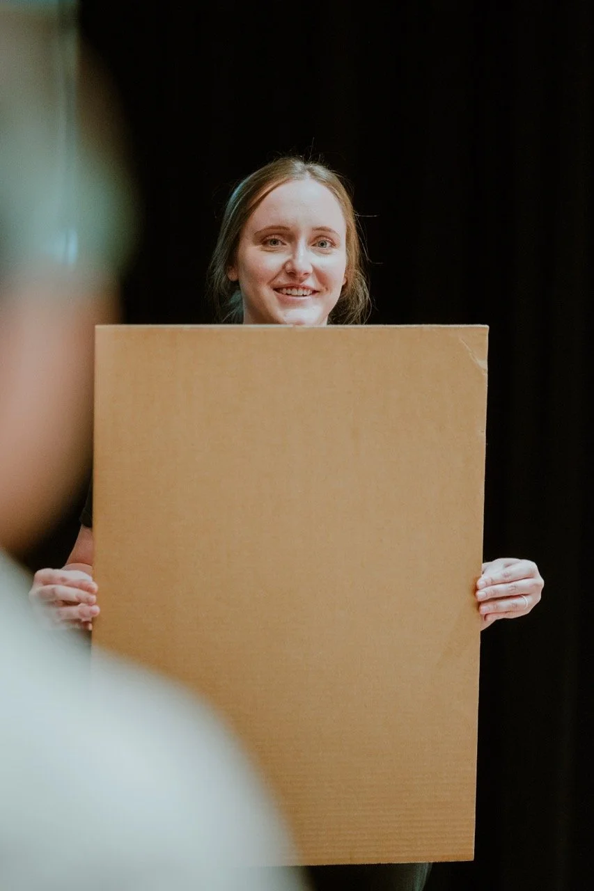 Person holding a large blank cardboard against a dark background.