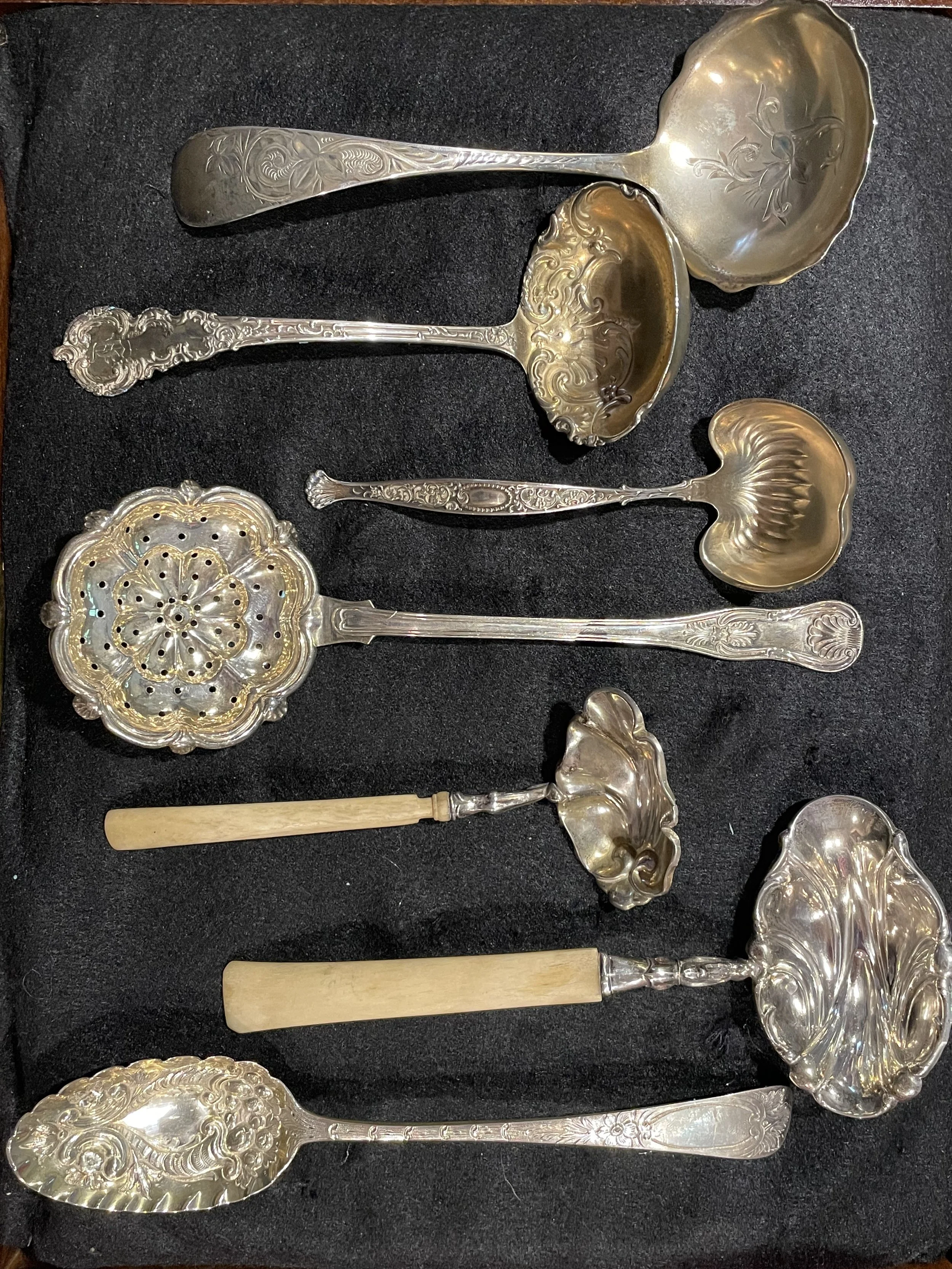 An exquisite collection of ornate sterling silver serving ladles and a large pierced sifter spoon, some featuring elegant bone handles