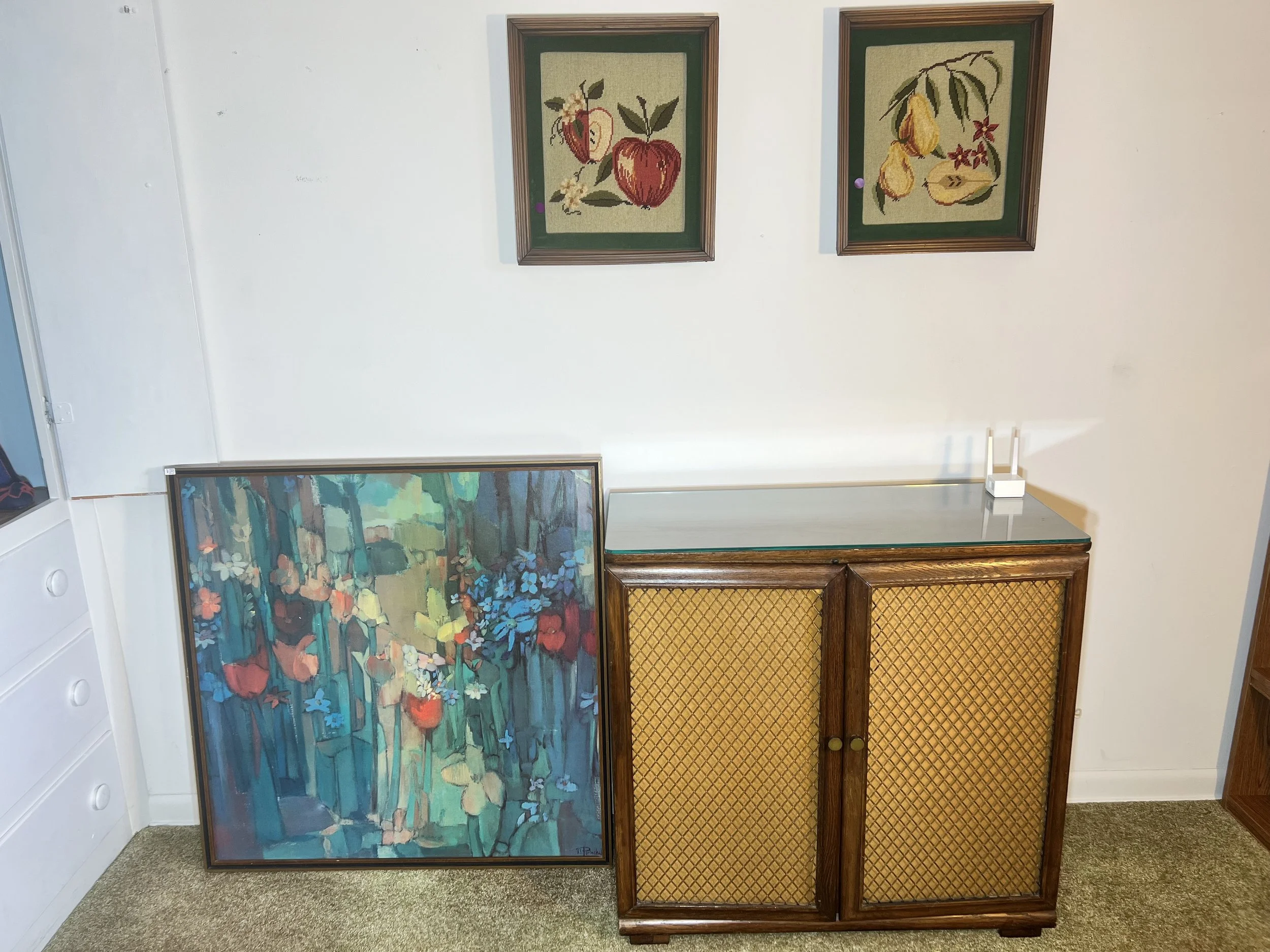 Retro wood cabinet with wicker-panel doors shown next to vibrant abstract floral art.