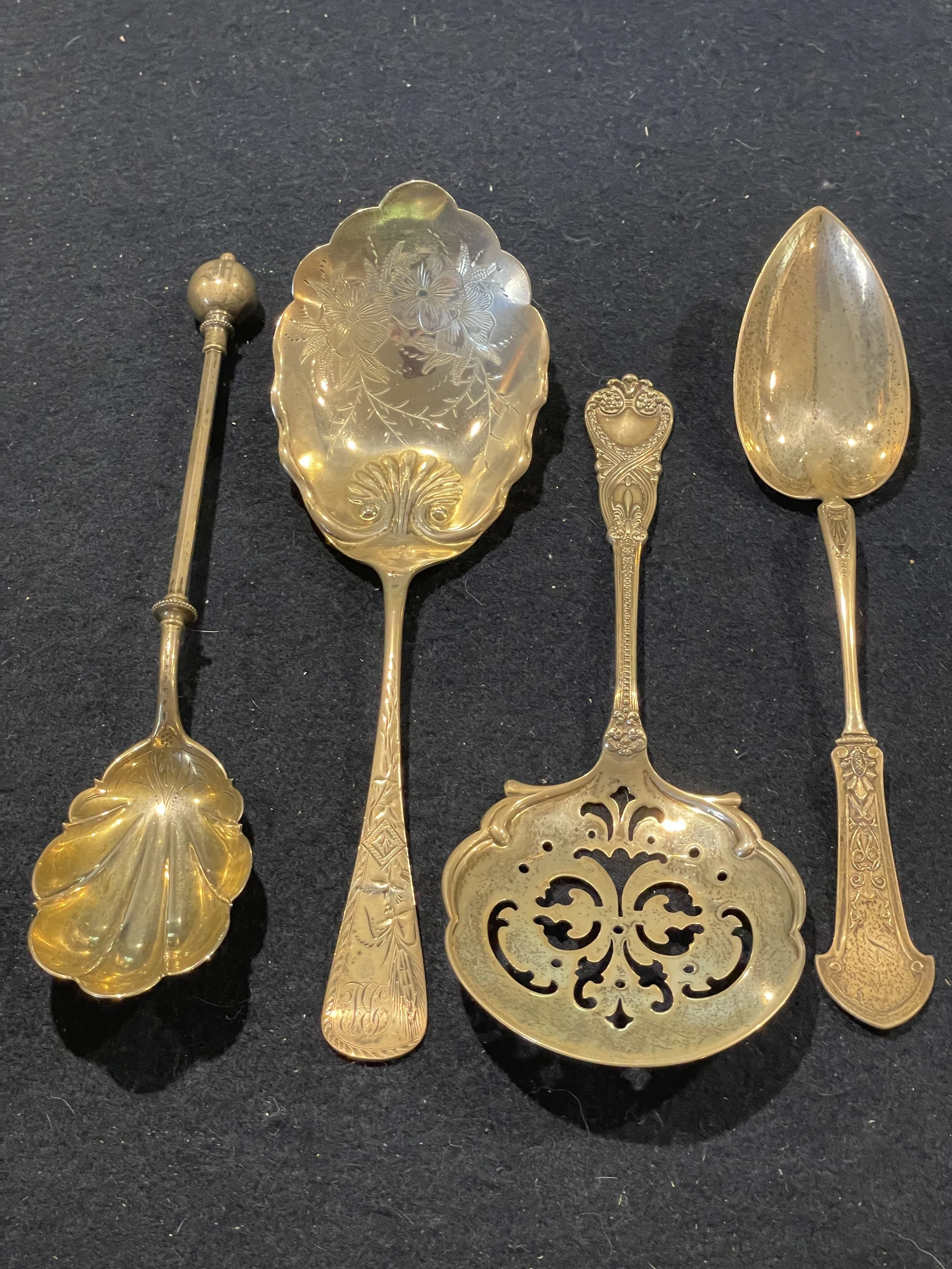 A stunning set of four gold-washed (vermeil) sterling silver serving spoons featuring intricate floral engravings and a shell-motif bowl