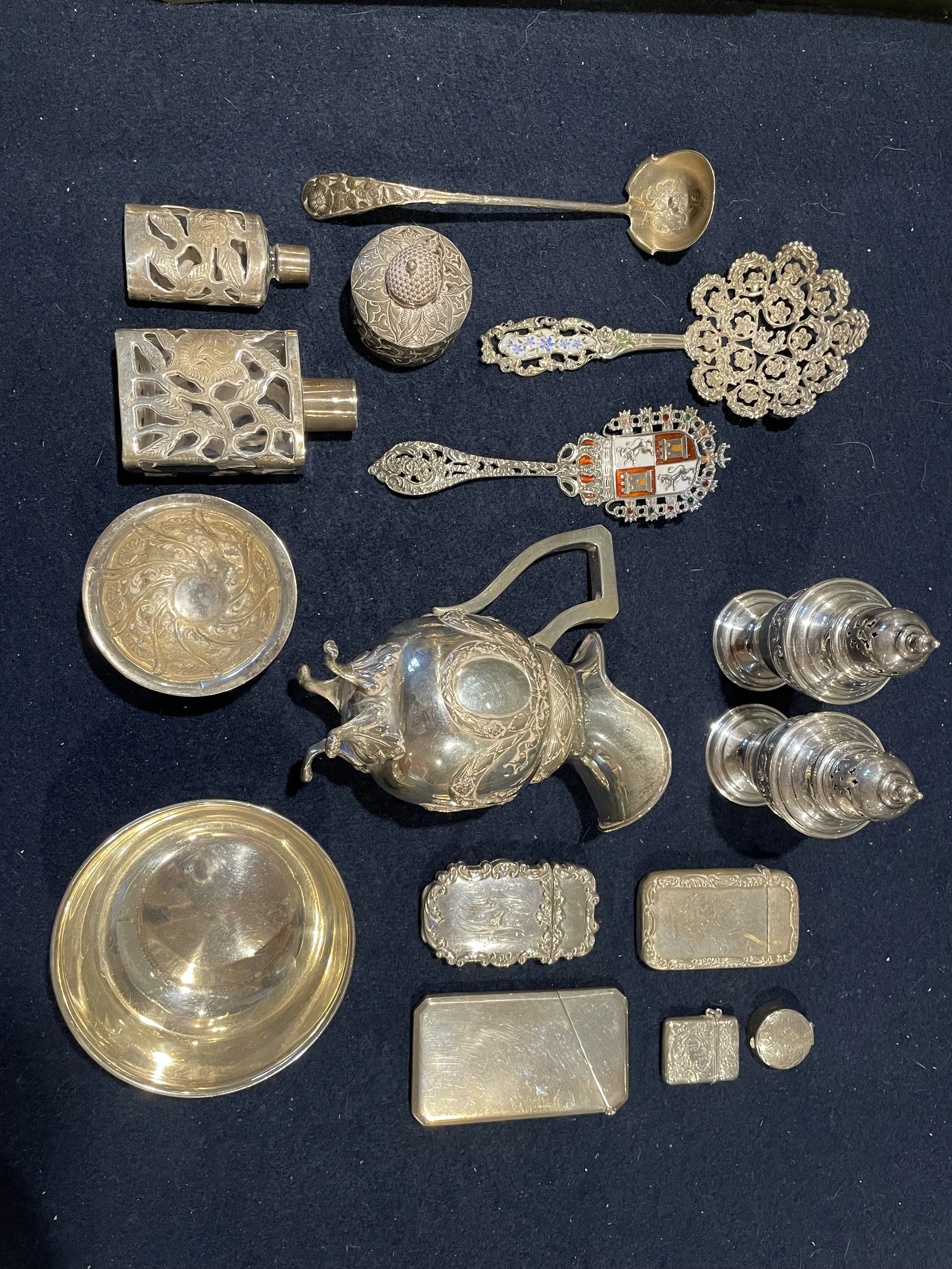 A premier assortment of sterling silver smalls, including silver-clad glass scent bottles, ornate heraldic spoons with enamel crests, and vintage match safes