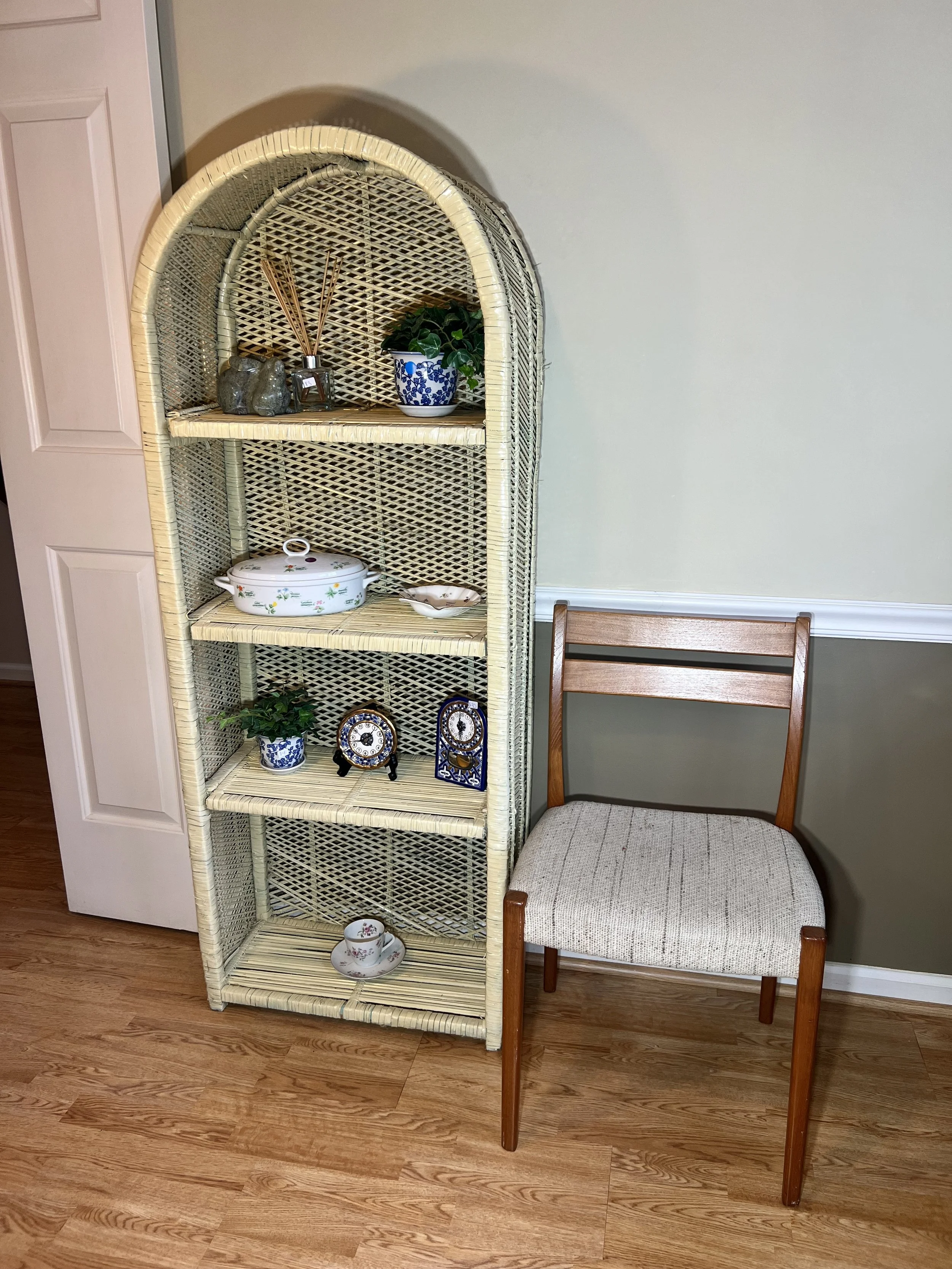 A classic cream-painted wicker shelf featuring an elegant arched top and intricate latticework, shown with decorative blue and white porcelain and collectible mantle clocks