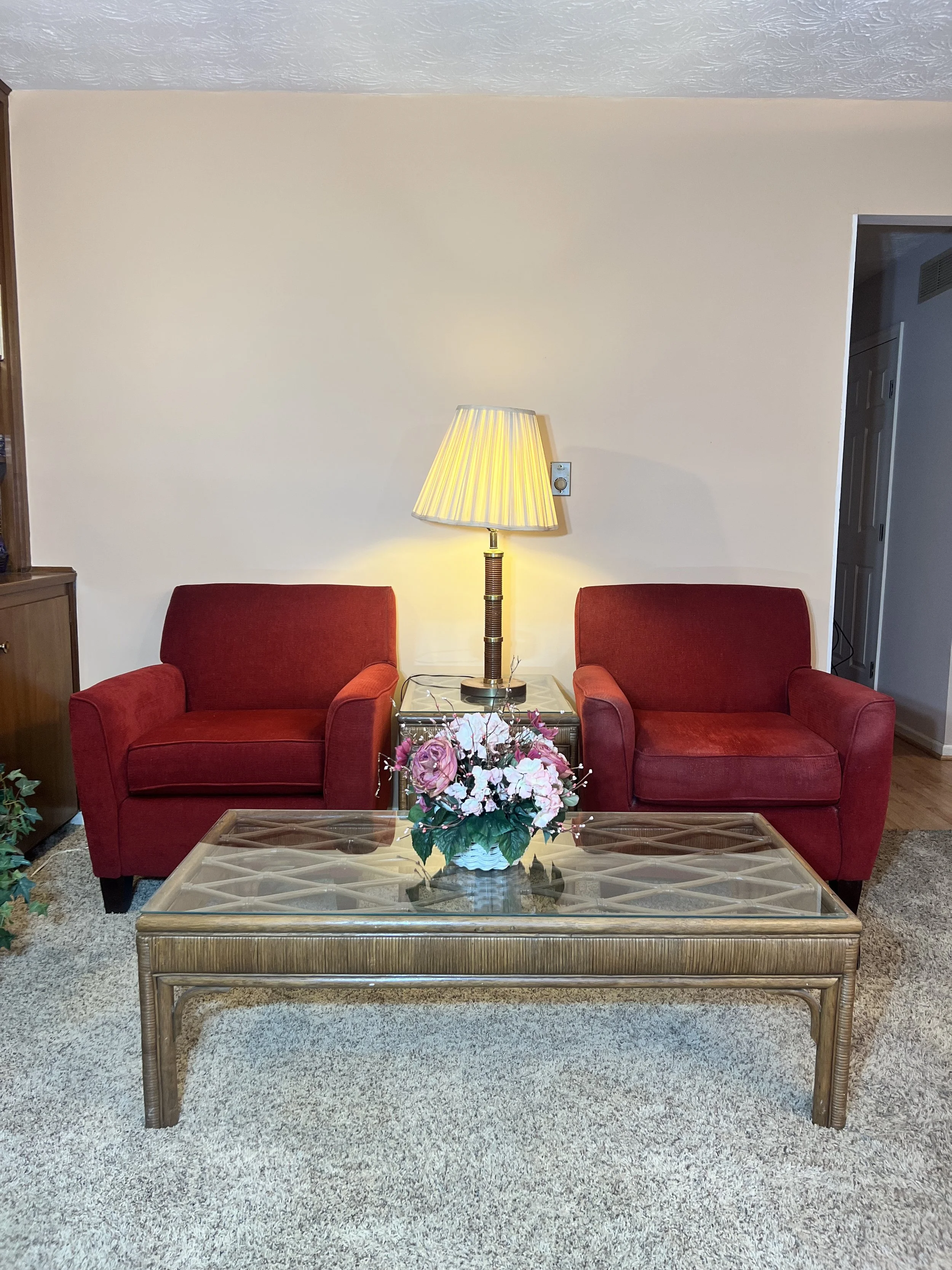 Red upholstered armchairs flanking a glass-top rattan coffee table with a decorative lattice design
