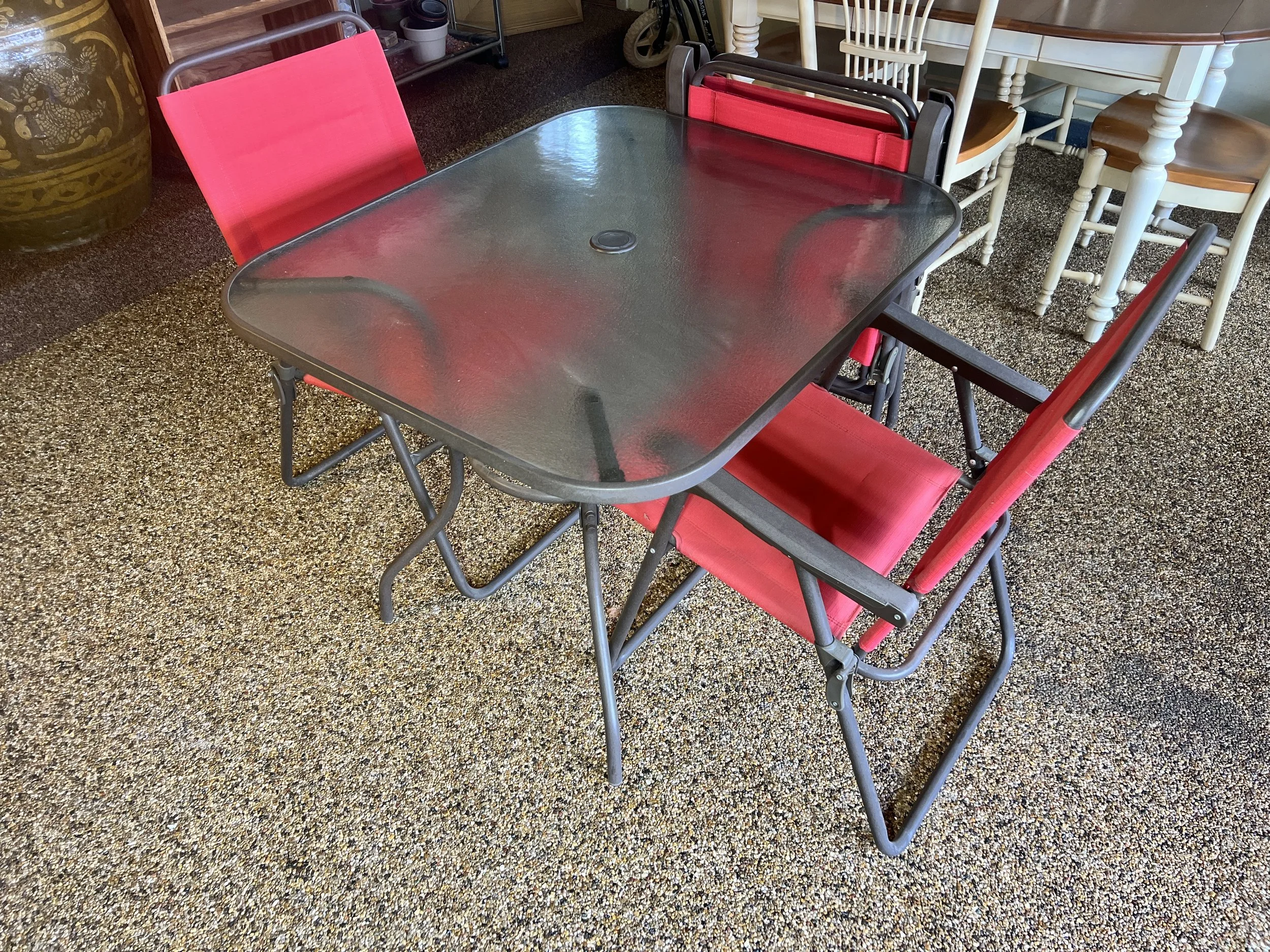 Outdoor bistro set featuring a square glass-top table and red mesh folding chairs
