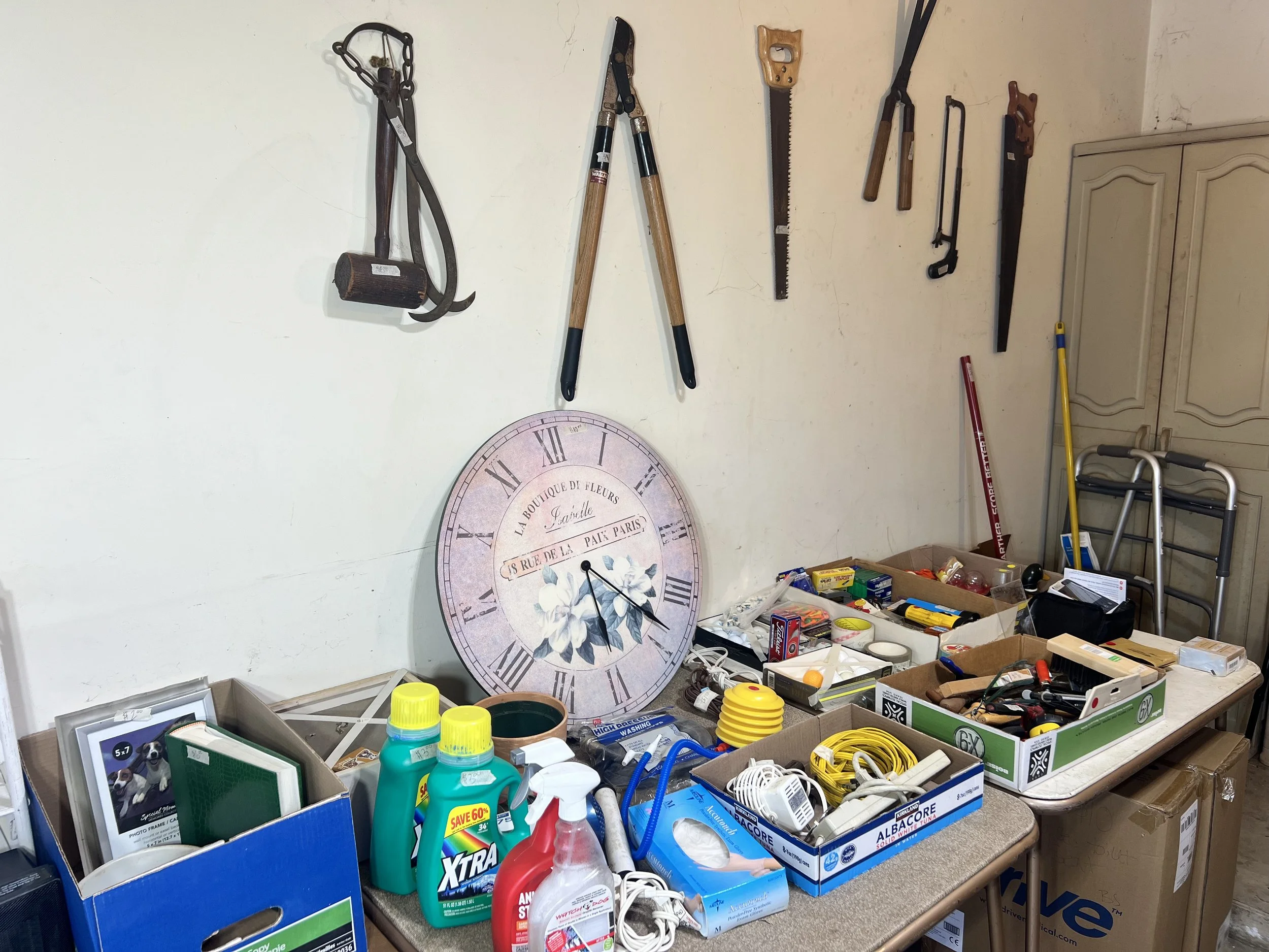 Garden Tools & Home Goods – Large wall clock, heavy-duty loppers, hand saws, and assorted household cleaning supplies and hardware