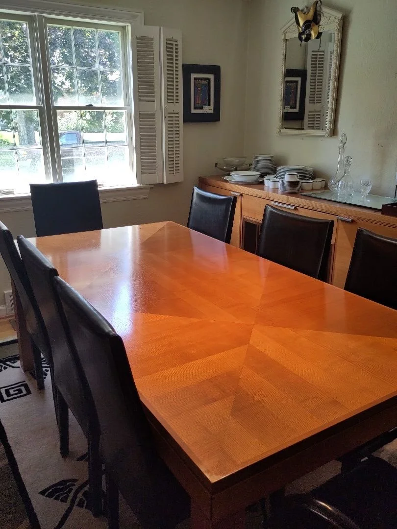 Designer wood dining table showcasing a starburst veneer top, matching short buffet. Table surrounded by six luxury black leather high-back chairs by Arper Italy.