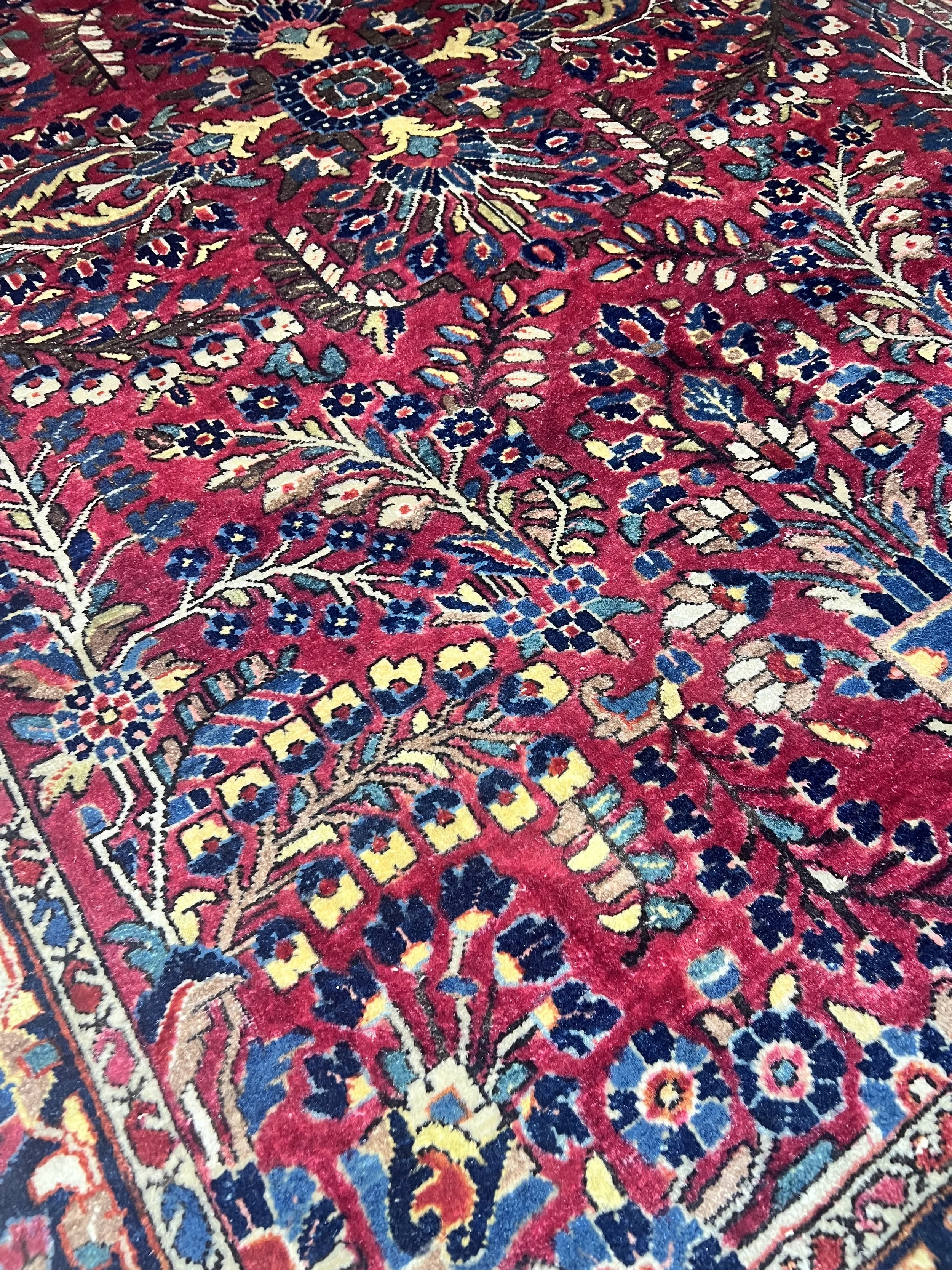 A beautiful hand-knotted wool area rug featuring a vibrant red field with intricate floral "Tree of Life" and medallion patterns