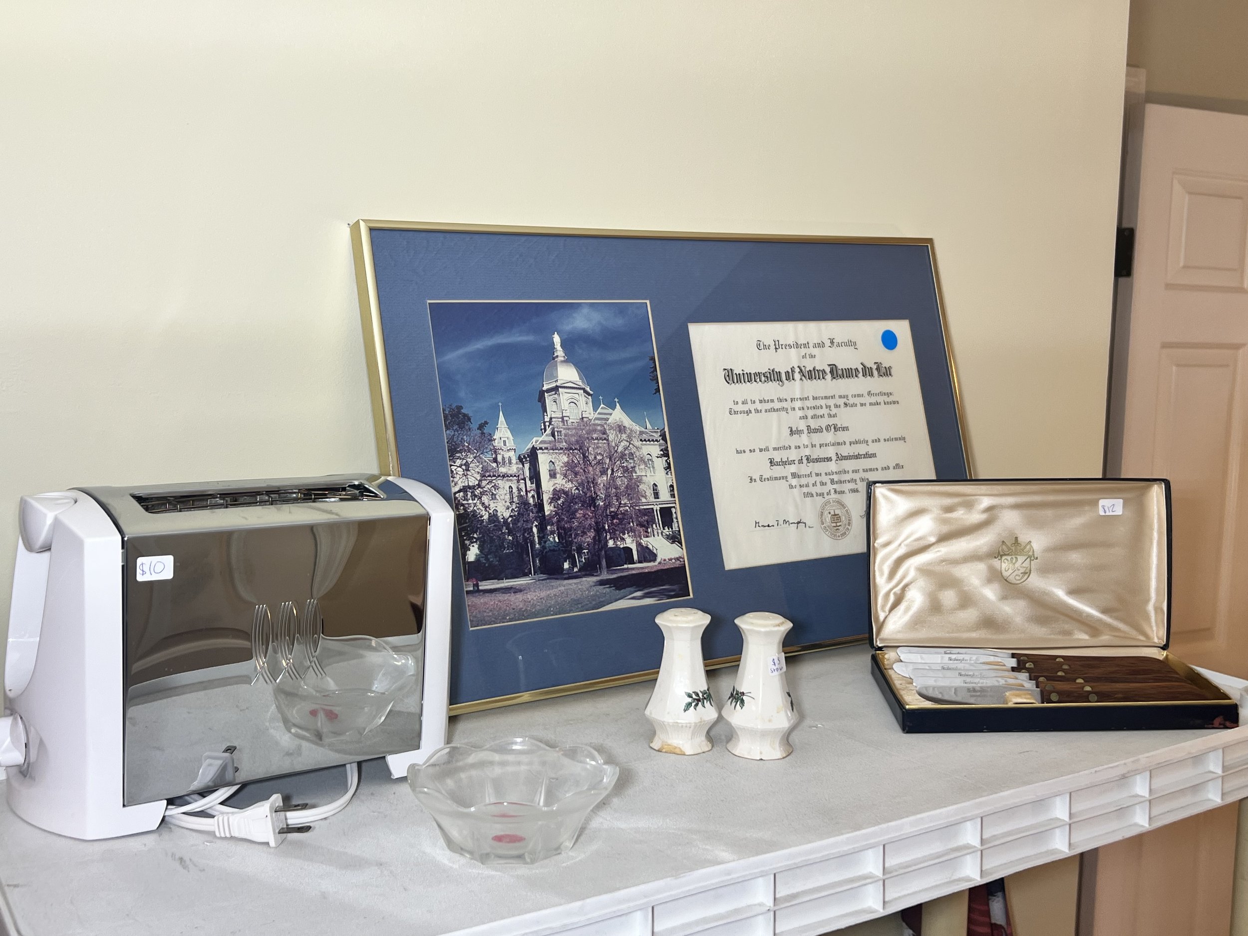 A framed University of Notre Dame diploma, a modern chrome toaster, ceramic salt and pepper shakers, and a boxed steak knife set