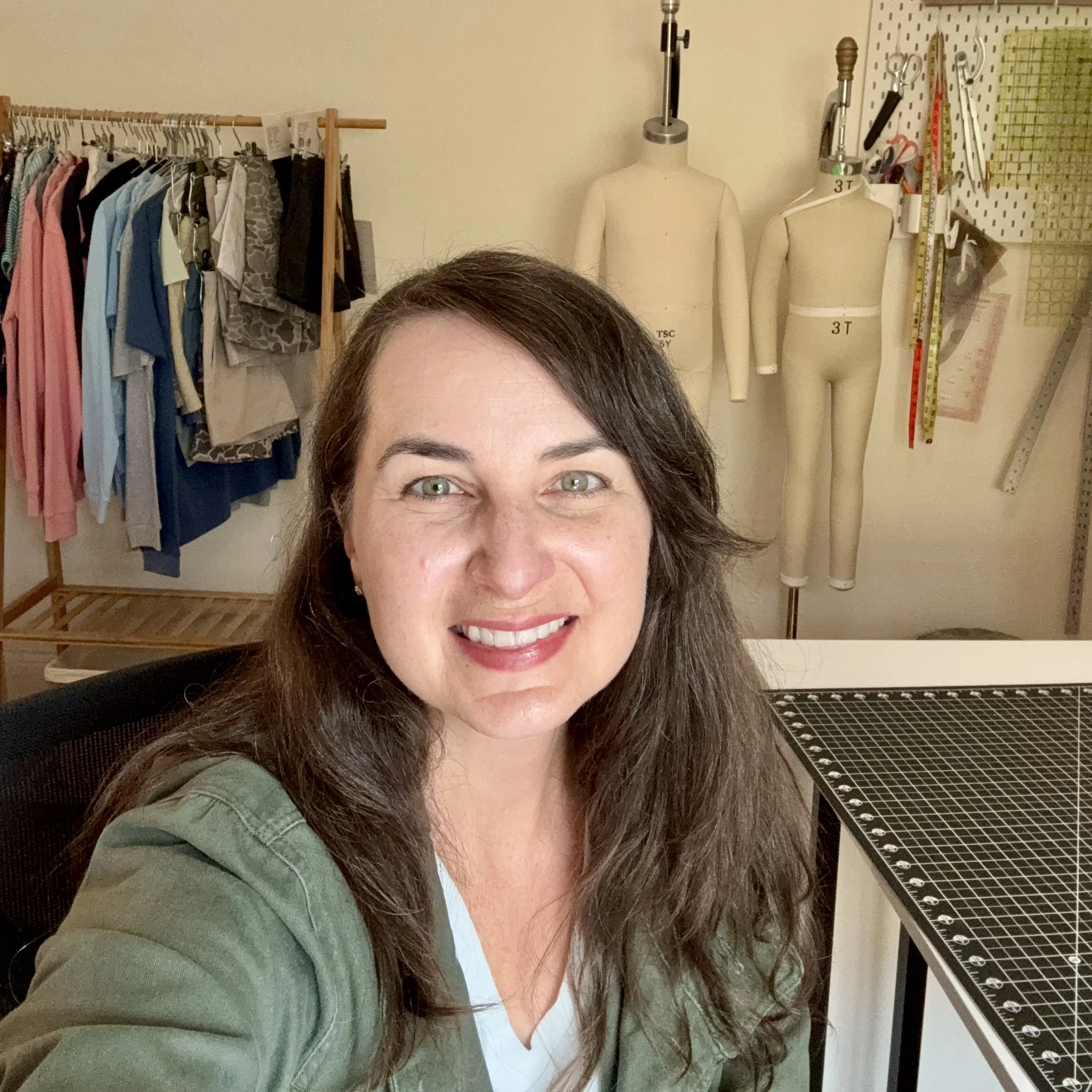 A woman with dark hair smiling, garment rack & children's dress forms in the background