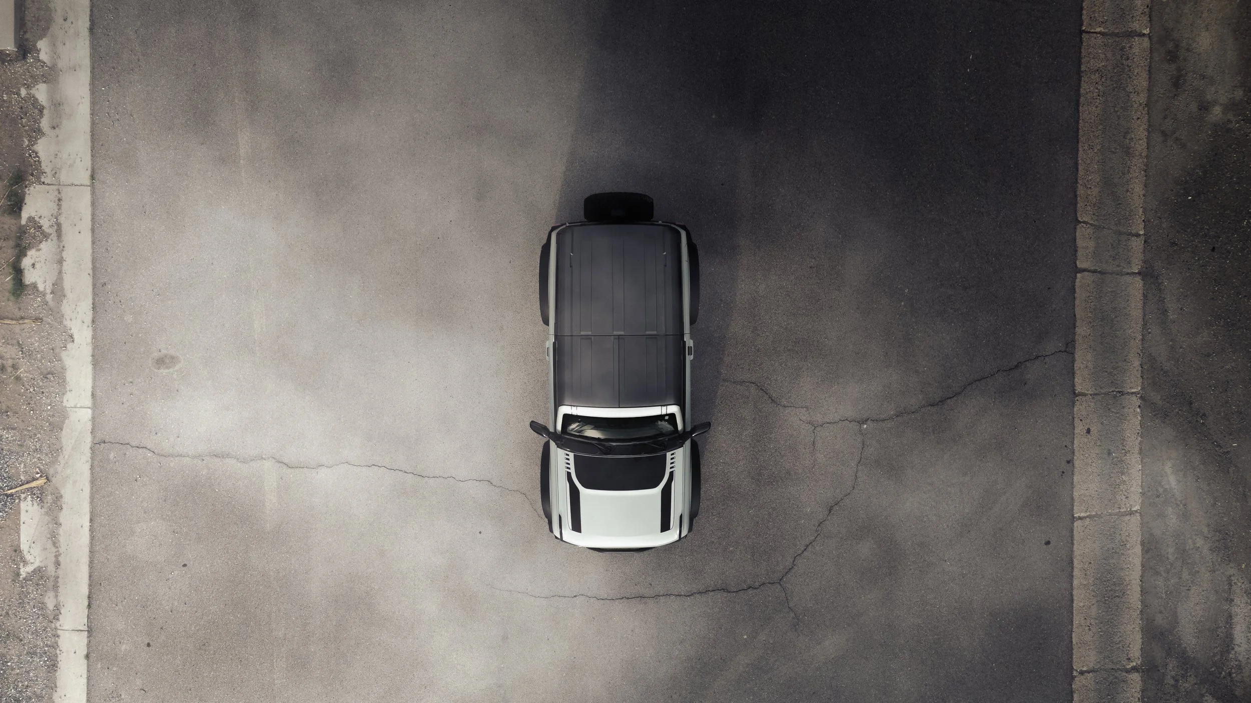 Top-down view of a black and white SUV parked on a cracked asphalt parking lot.