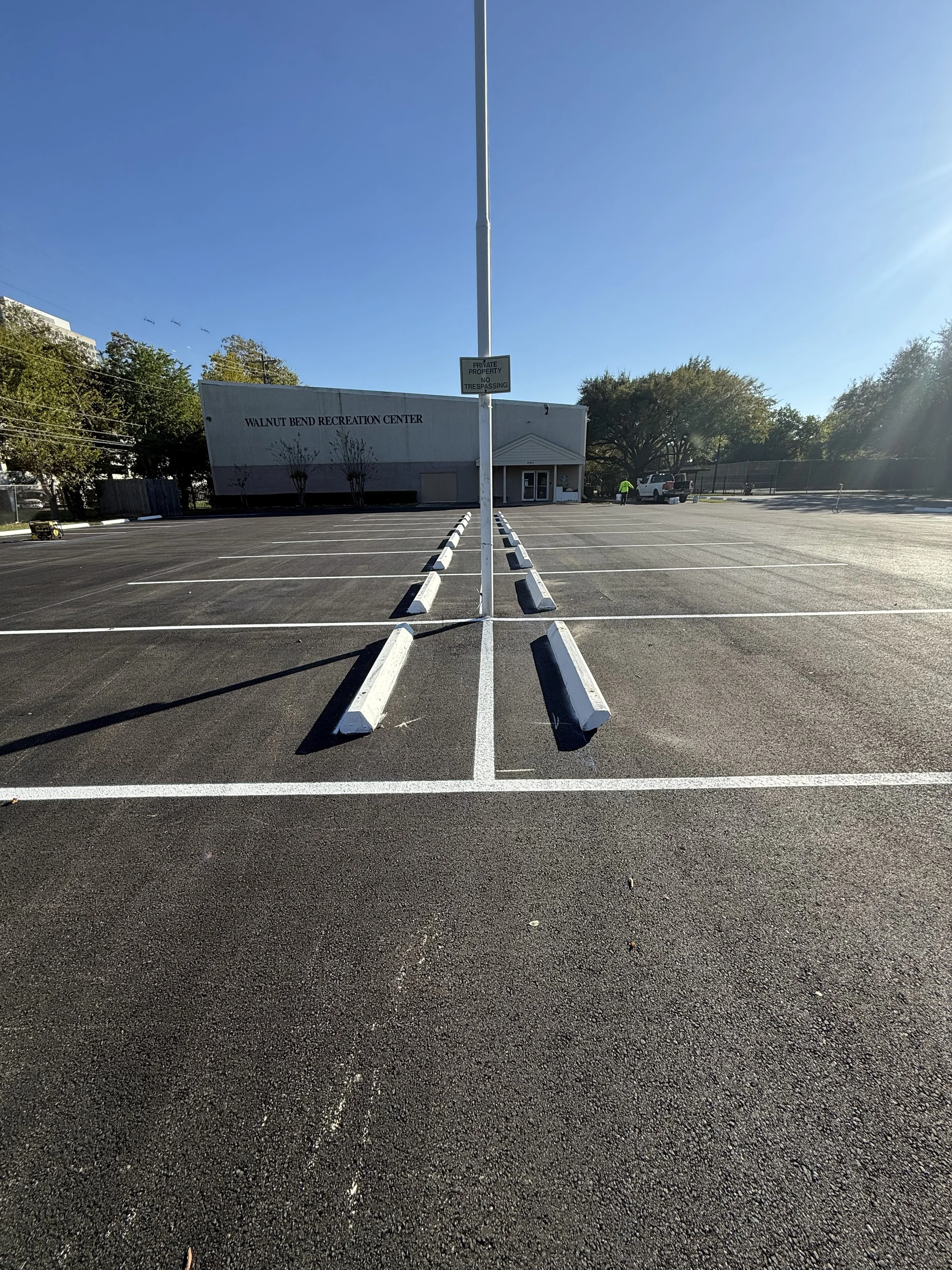Empty parking lot in front of Walnut Bend Recreation Center with marked parking spaces, a white building, and a clear blue sky.