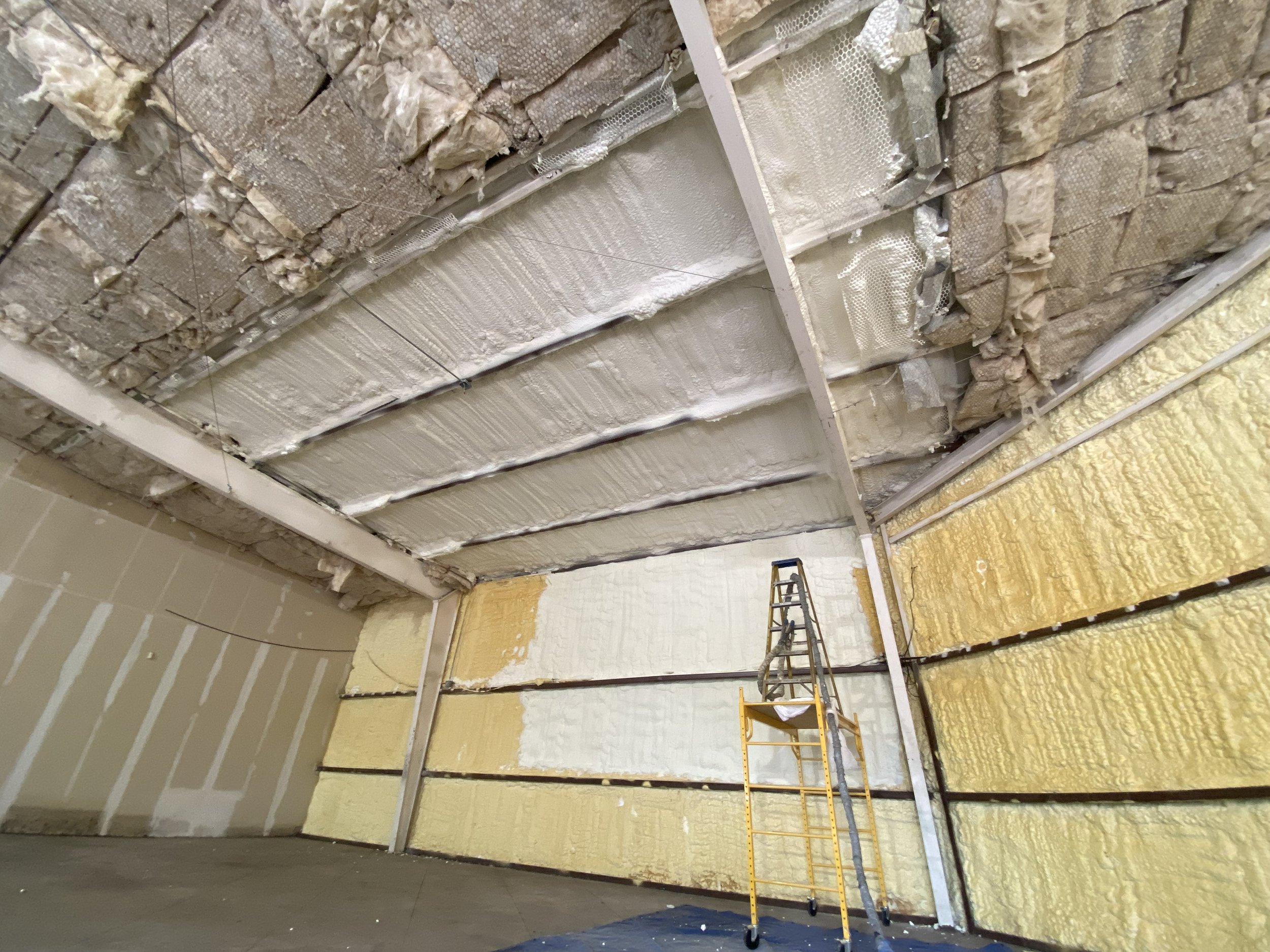 Insulated walls and ceiling under construction with spray foam insulation and metal framing, ladder in the room.