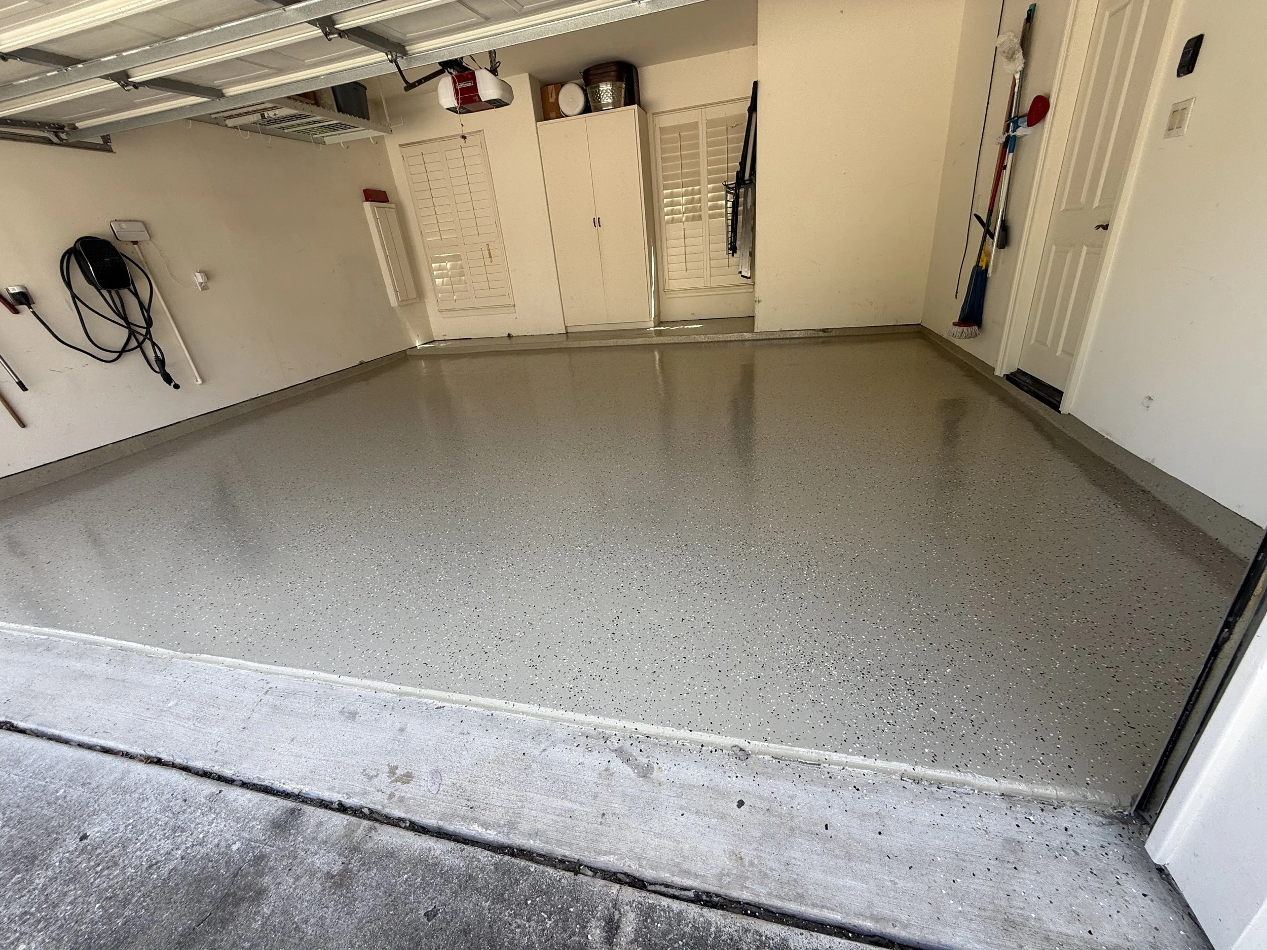 Empty residential garage with polished epoxy floor, garage door open, and various tools and storage cabinets along the wall.