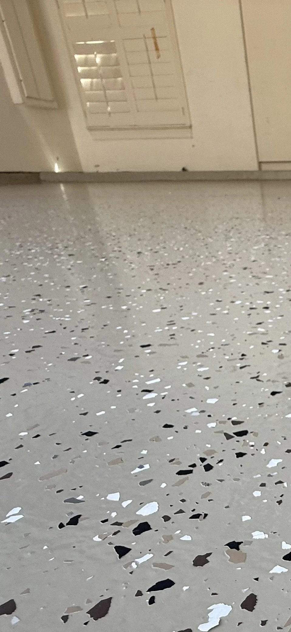 Close-up view of a terrazzo floor with various colored chips, with a part of a door and a wall in the background.