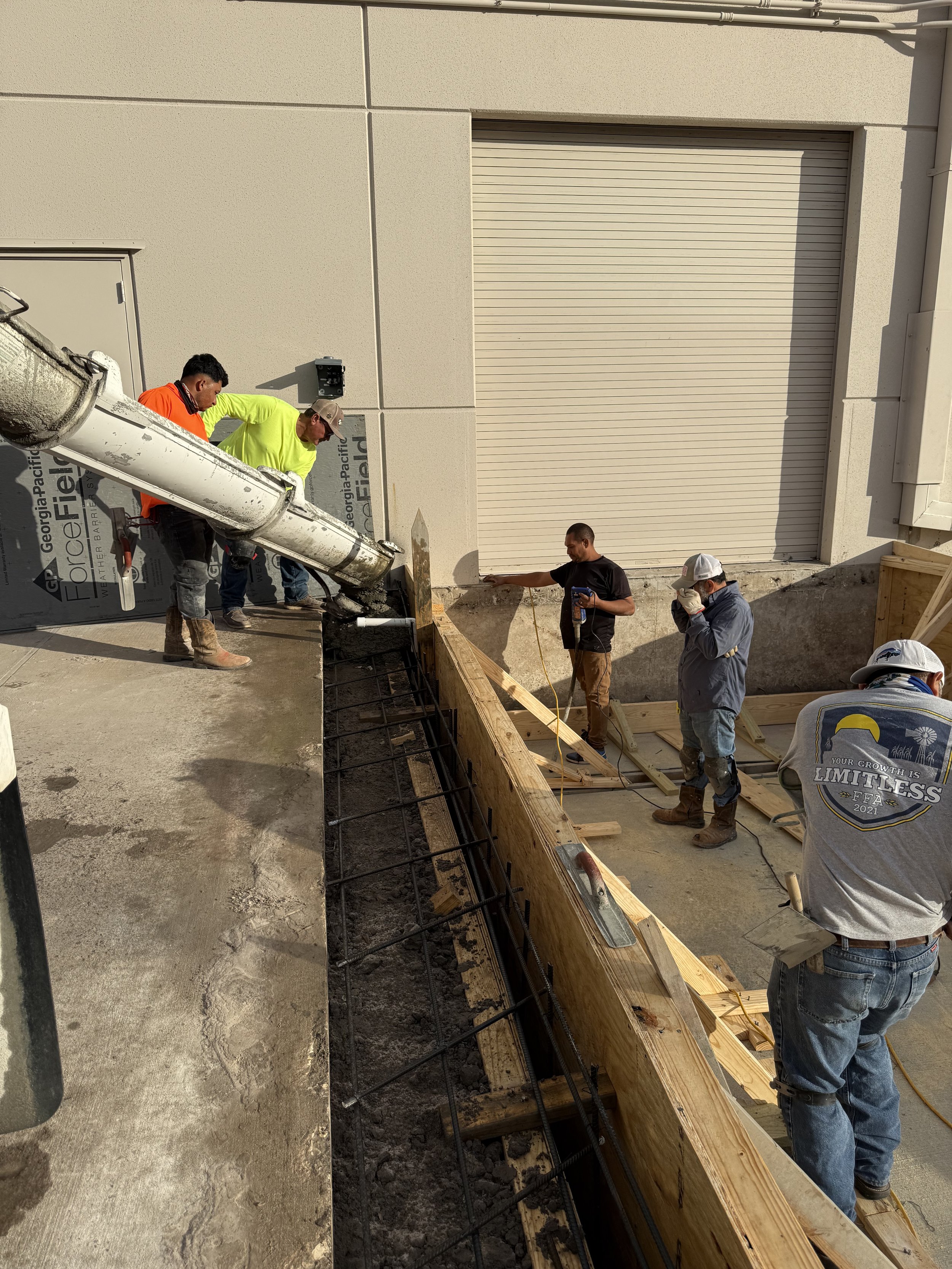 Construction workers pouring concrete into a wooden form for a building foundation.