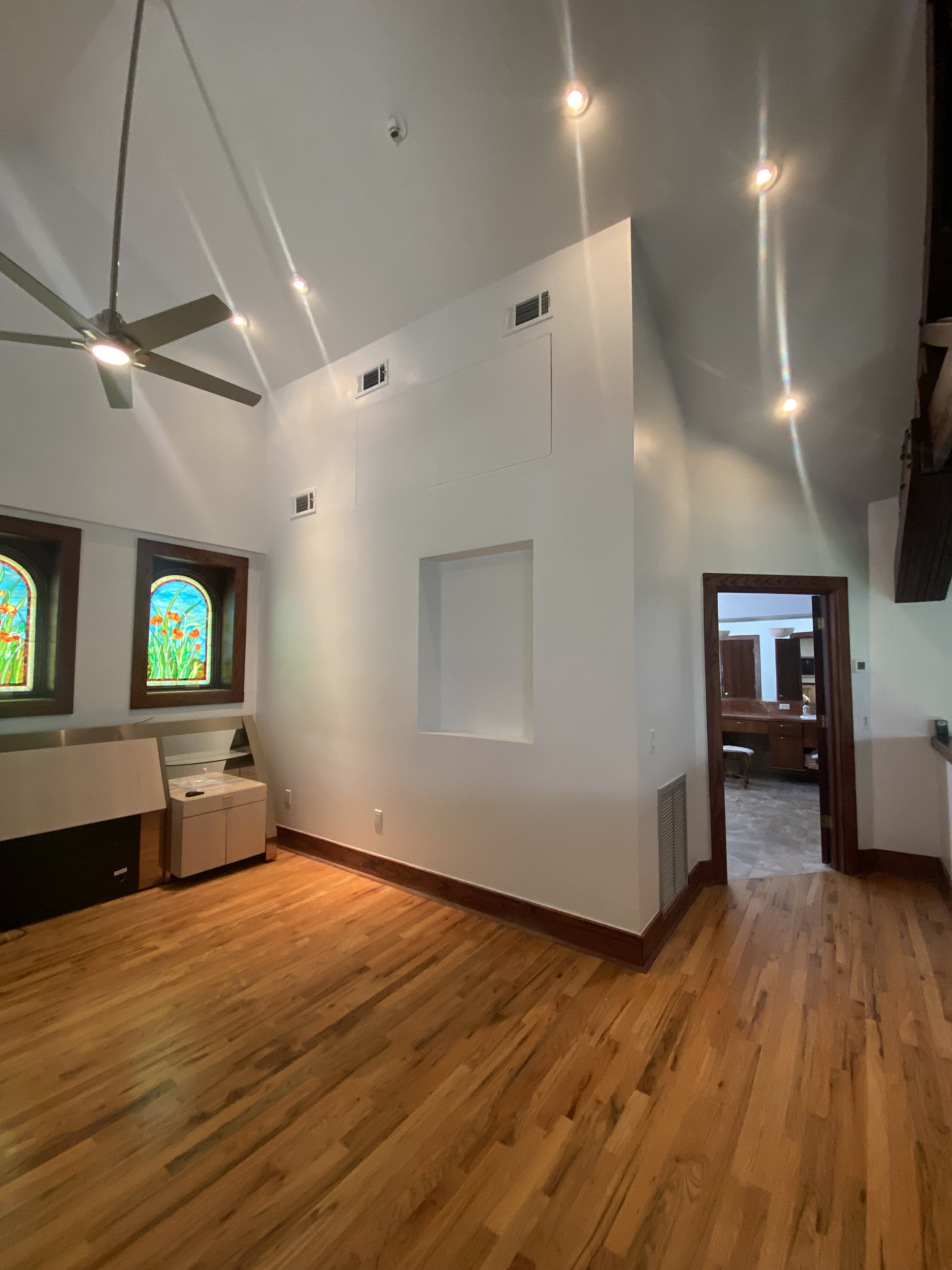 Interior view of a room with wooden floors, white walls, ceiling fan, and stained glass windows.