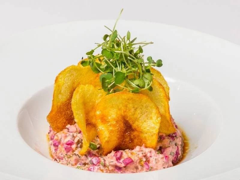 Gourmet dish with potato chips, microgreens, and a pink creamy salad on a white plate.
