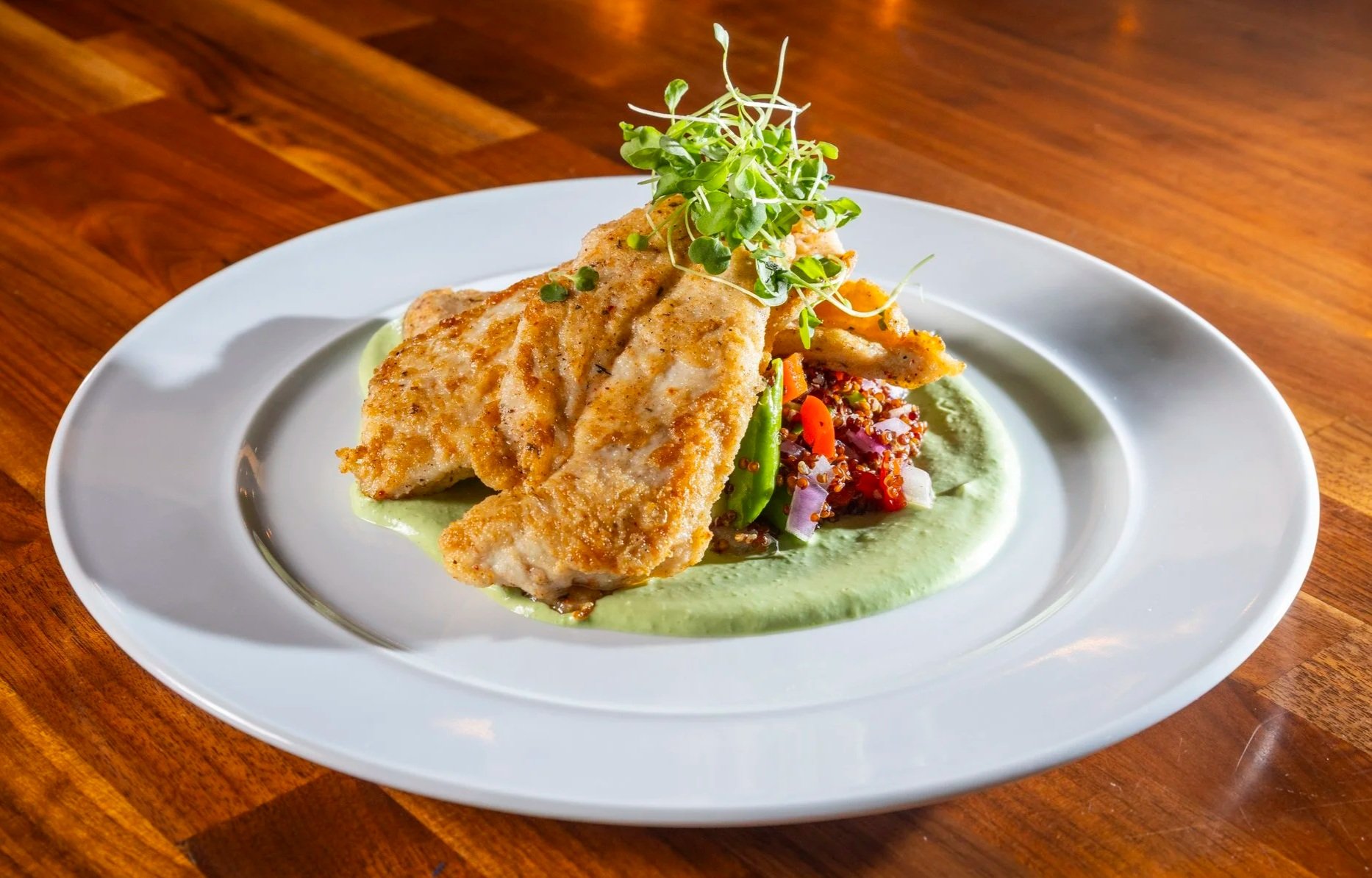 Pan-seared chicken breasts with vegetable quinoa, avocado yogurt sauce on a white oval plate