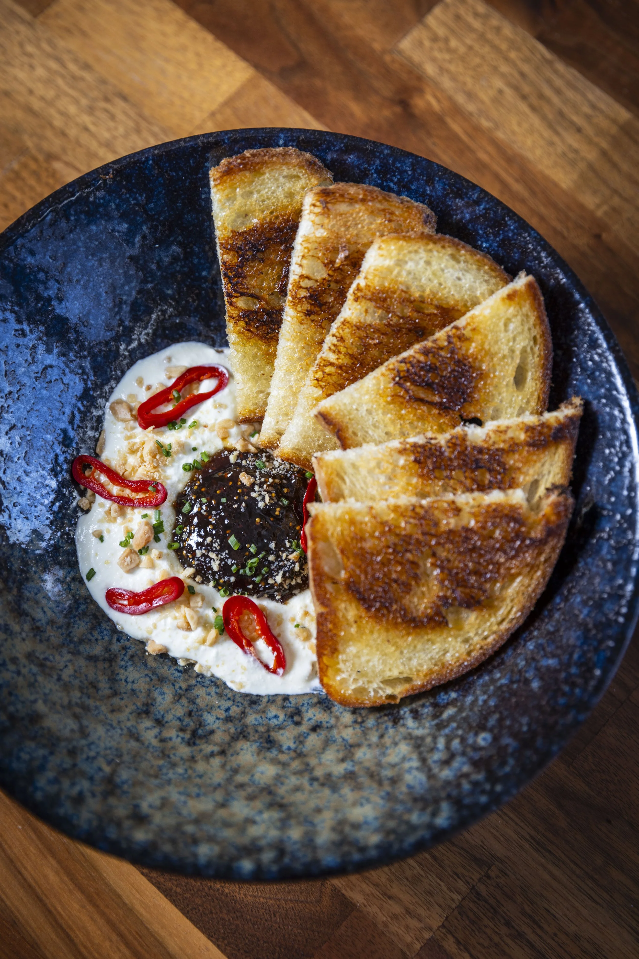 A black bowl containing whipped Feta with fig jam, pickled Fresno chiles, Marcona almonds, and sourdough crostinis. 