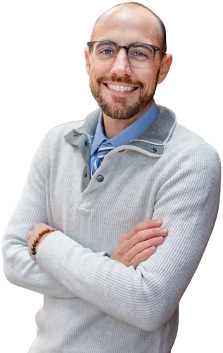 A smiling man with glasses, a beard, wearing a light gray sweater over a collared shirt and tie, crossing his arms.