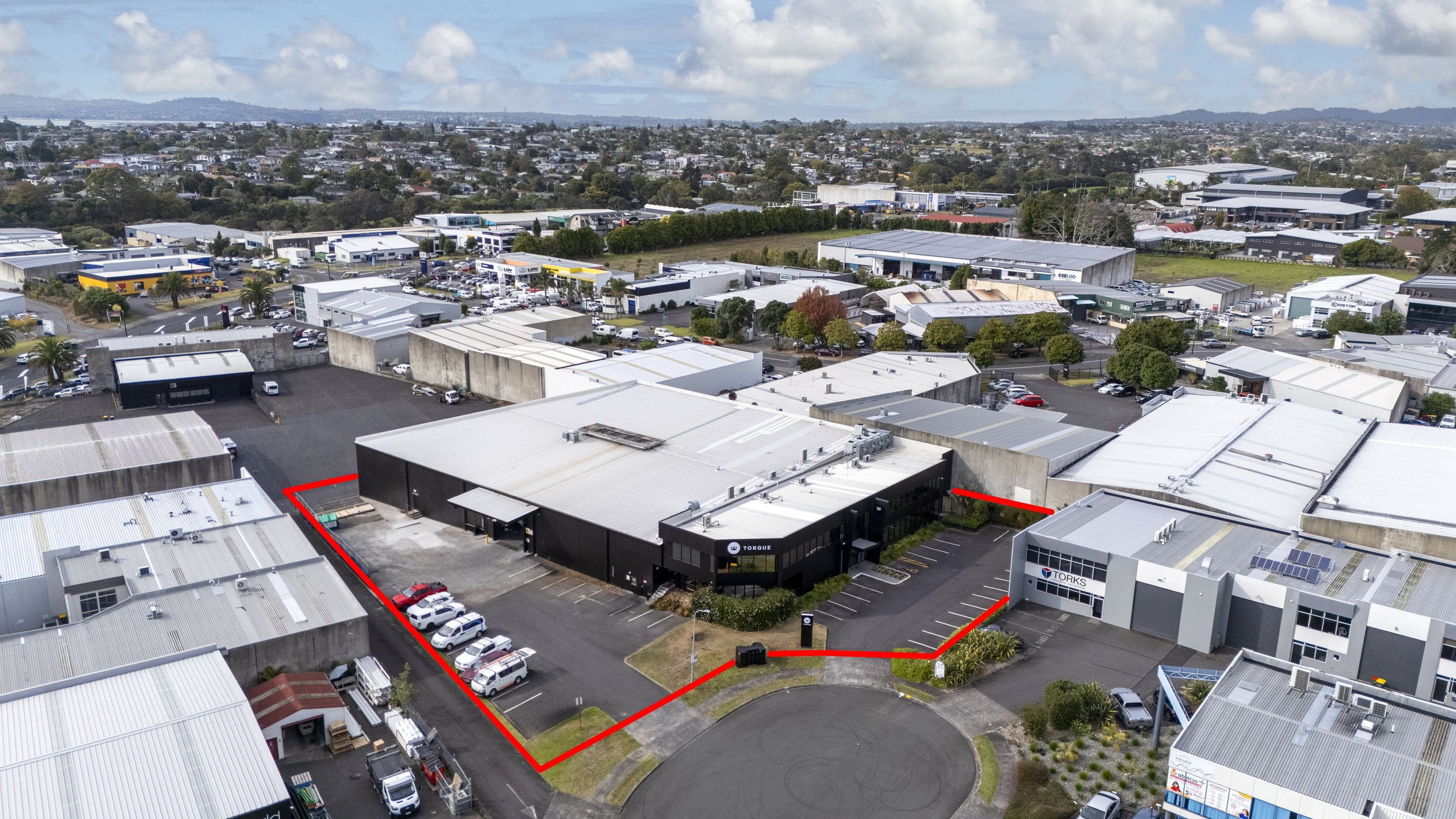 Aerial view of a commercial industrial area with buildings, parking lots, and streets, bordered by a red outline.