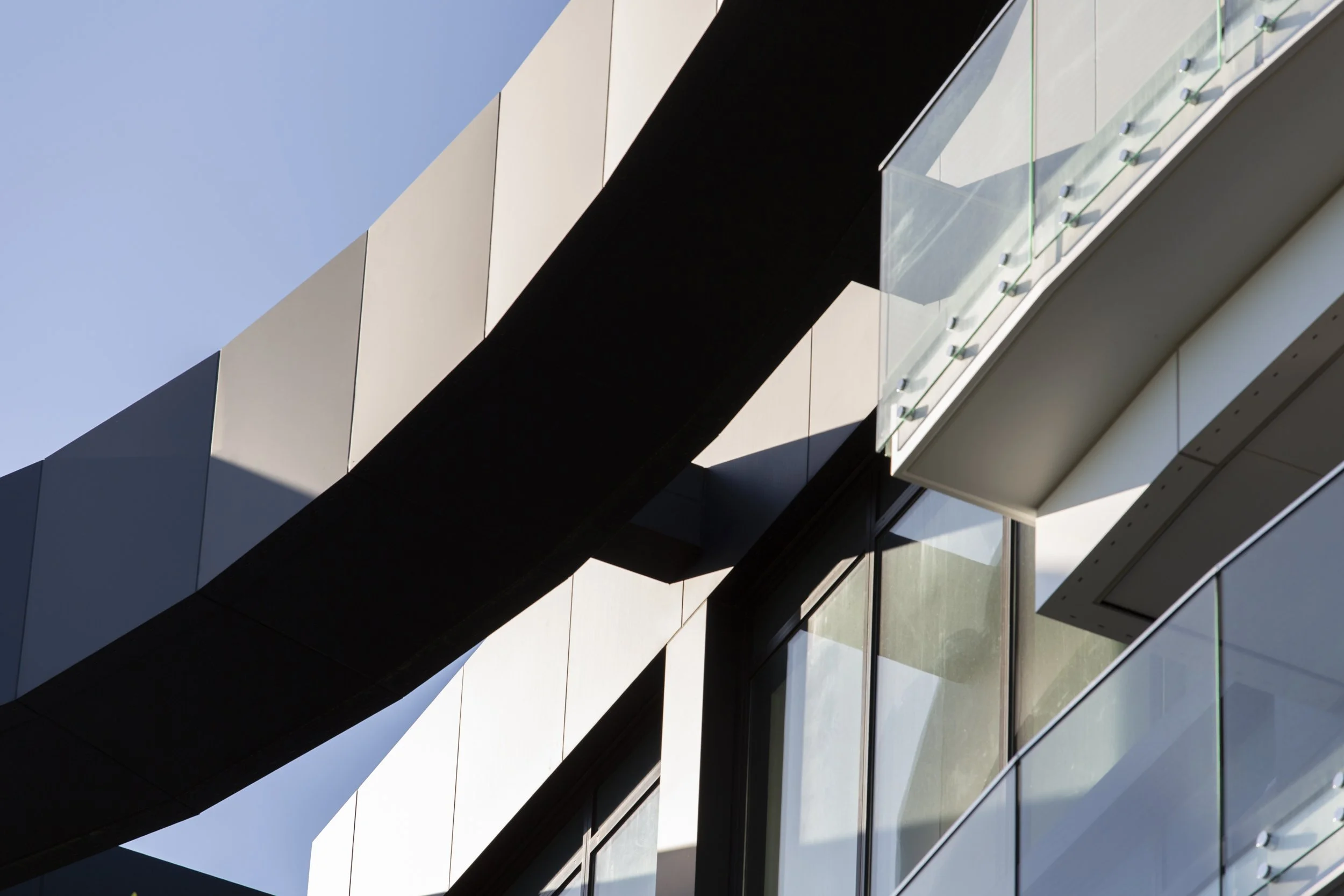 Close-up of a modern building with geometric shapes, glass and metal panels, and architectural details in sunlight.