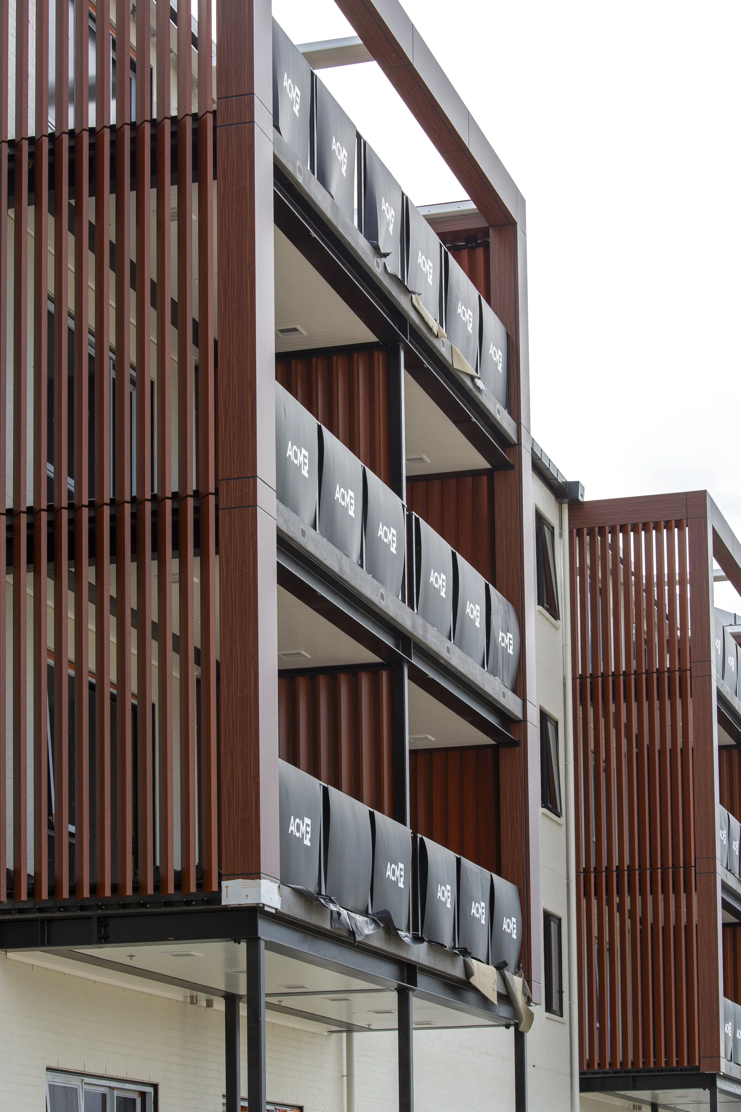 A multi-story building under construction featuring wooden exterior paneling and black ACME-branded construction barriers on the balconies.