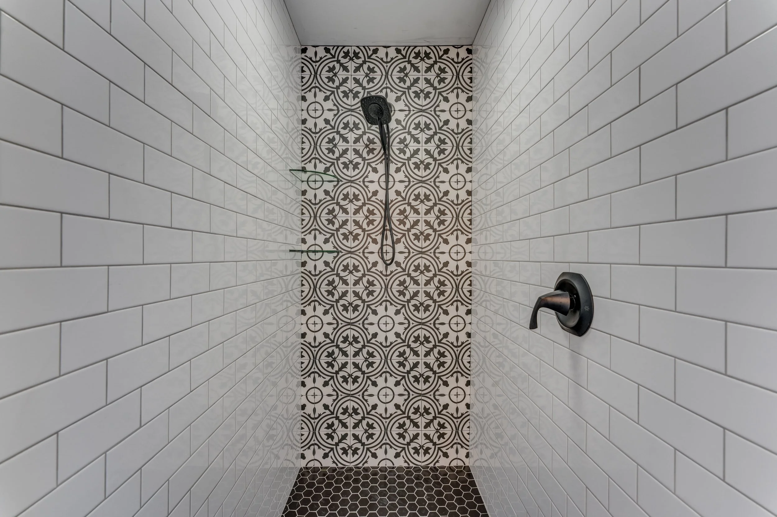 Shower interior with white subway tiles, patterned black and white wall tiles, black showerhead, and black faucet handle. Memphis real estate photography. 