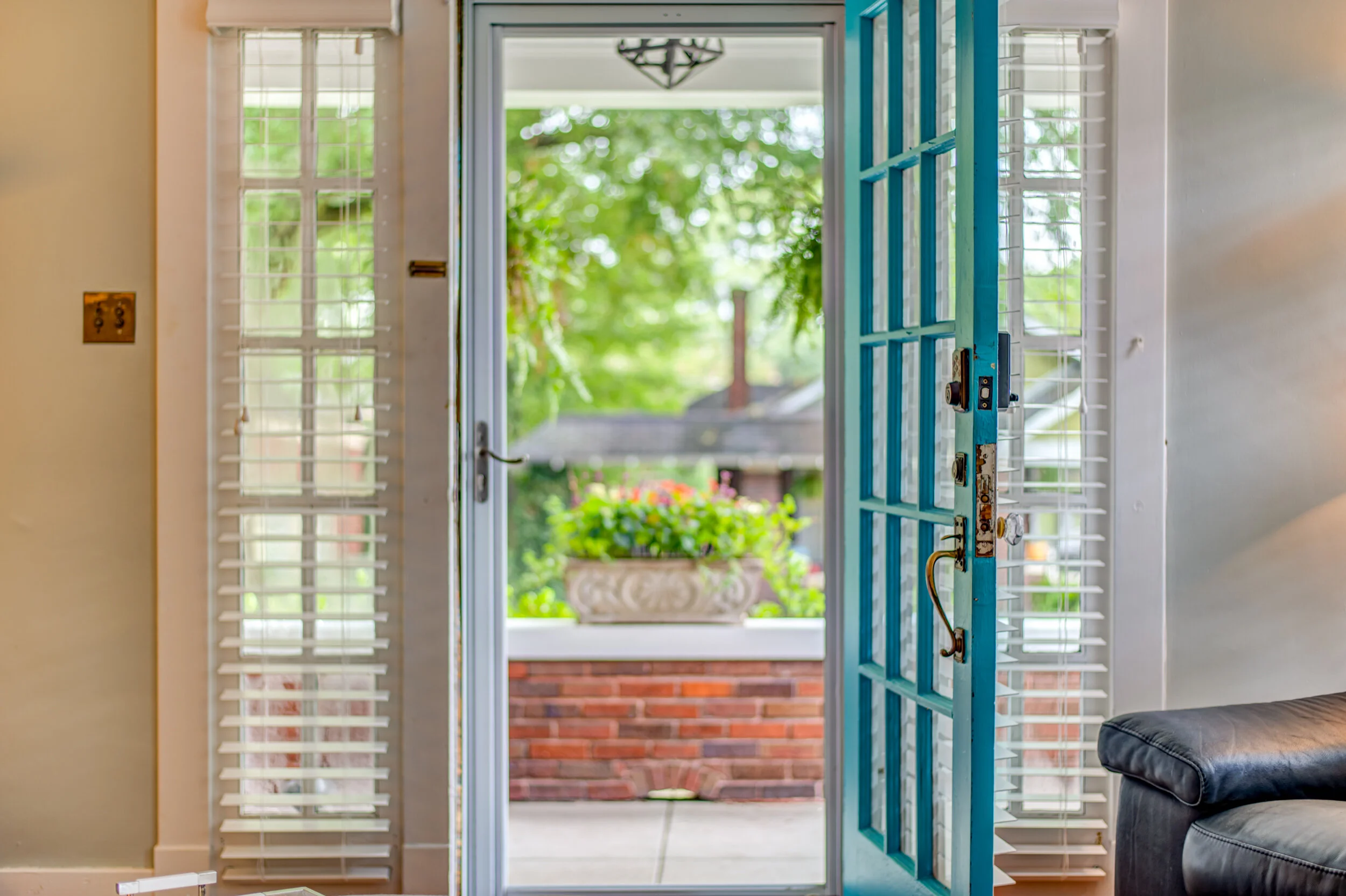 Interior view of a house door opening to a porch with green trees and a flower planter outside.