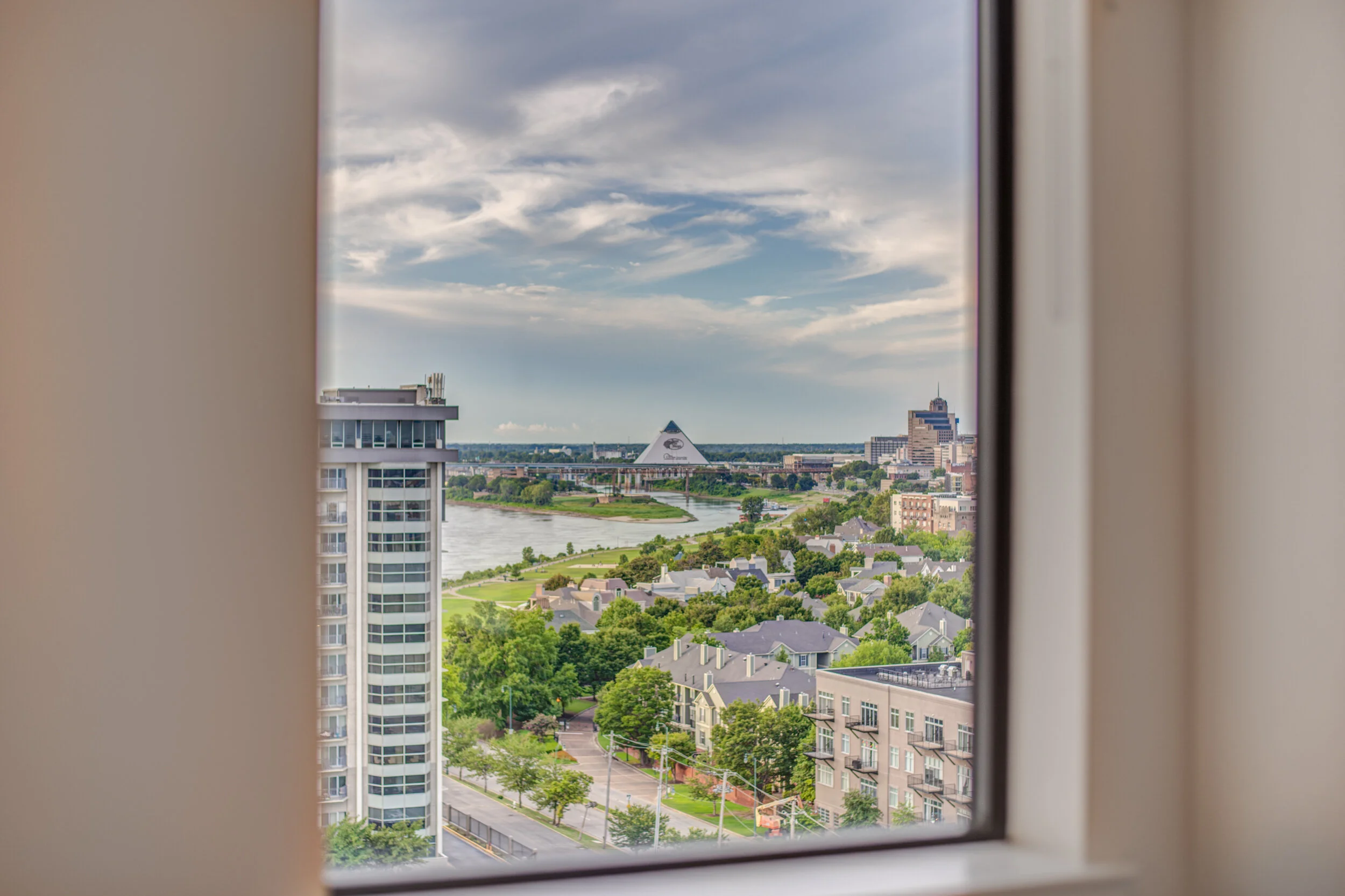 City skyline view through a window showing a river, modern buildings, and a partly cloudy sky. Memphis real estate photography. 