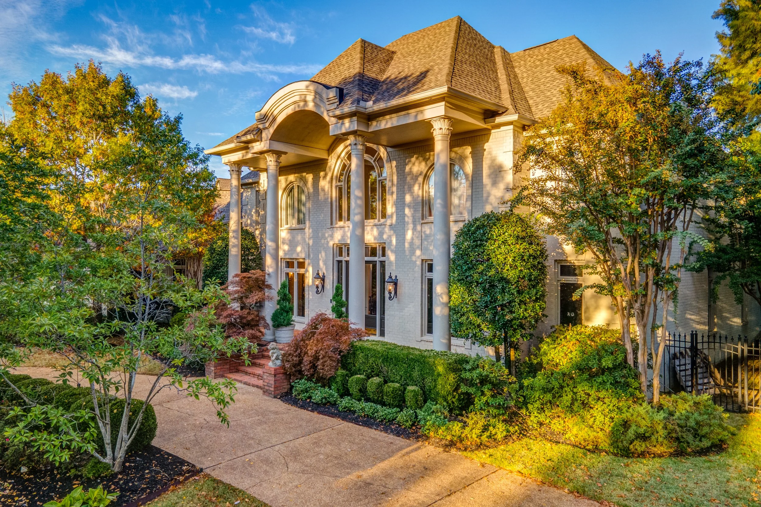 Front view of a large, elegant house with tall columns, arched windows, and lush landscaping in the sunlight. Memphis real estate photography. 
