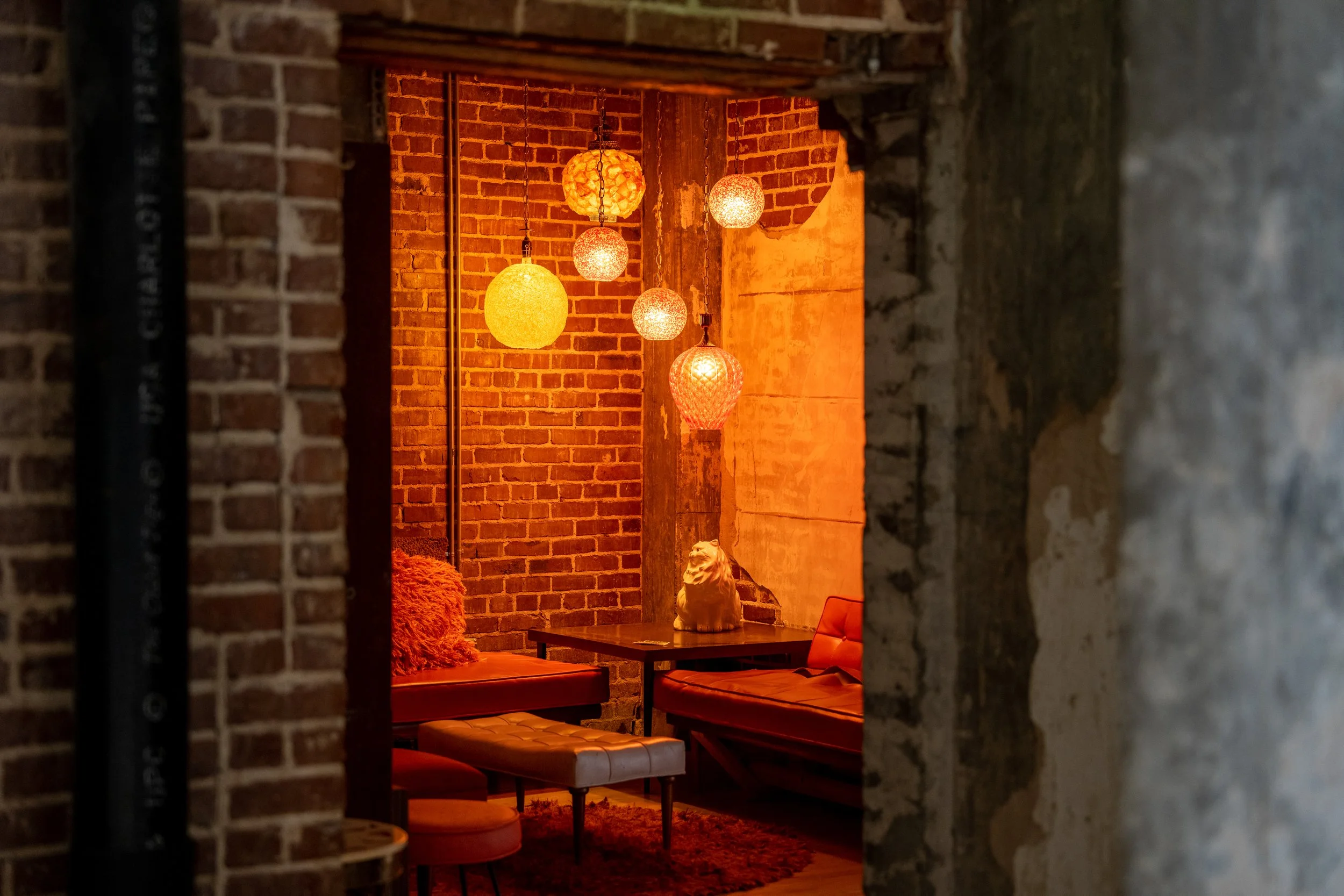 Cozy dining nook with brick walls, warm orange pendant lights, plush bench seating, and a decorative lion sculpture on the table. Memphis real estate photography. 
