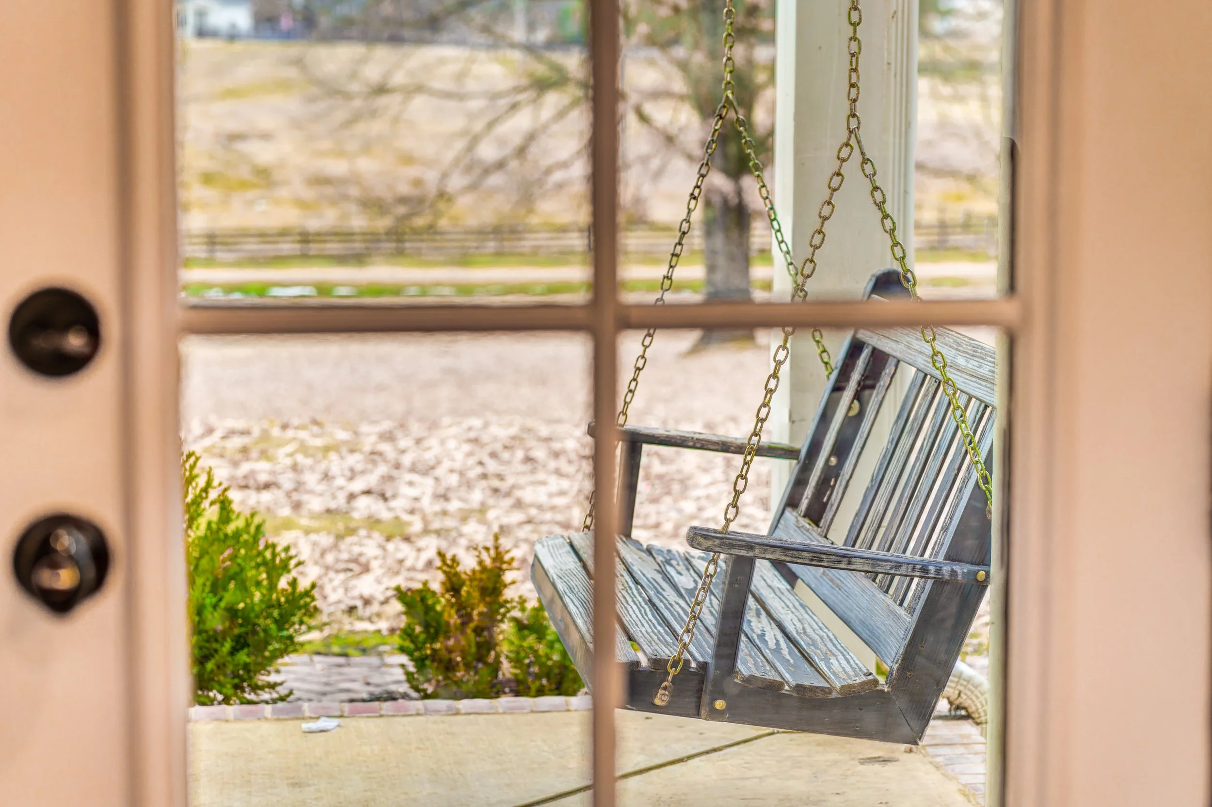 A porch swing hanging from chains on a porch, viewed through a window. Memphis real estate photography. 