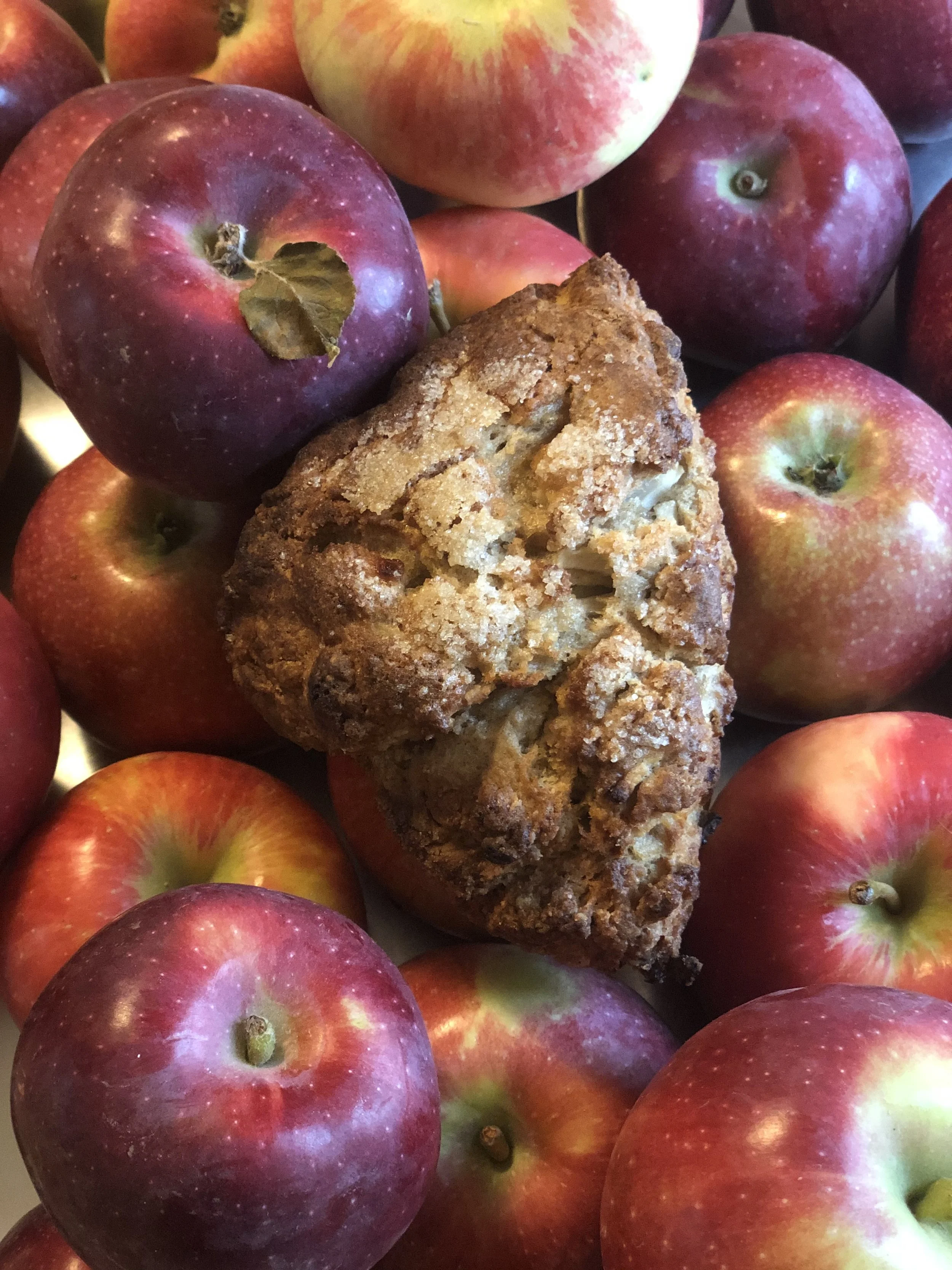 A collection of red and yellow apples surrounding a large, crumbly bread or muffin with a rough texture.