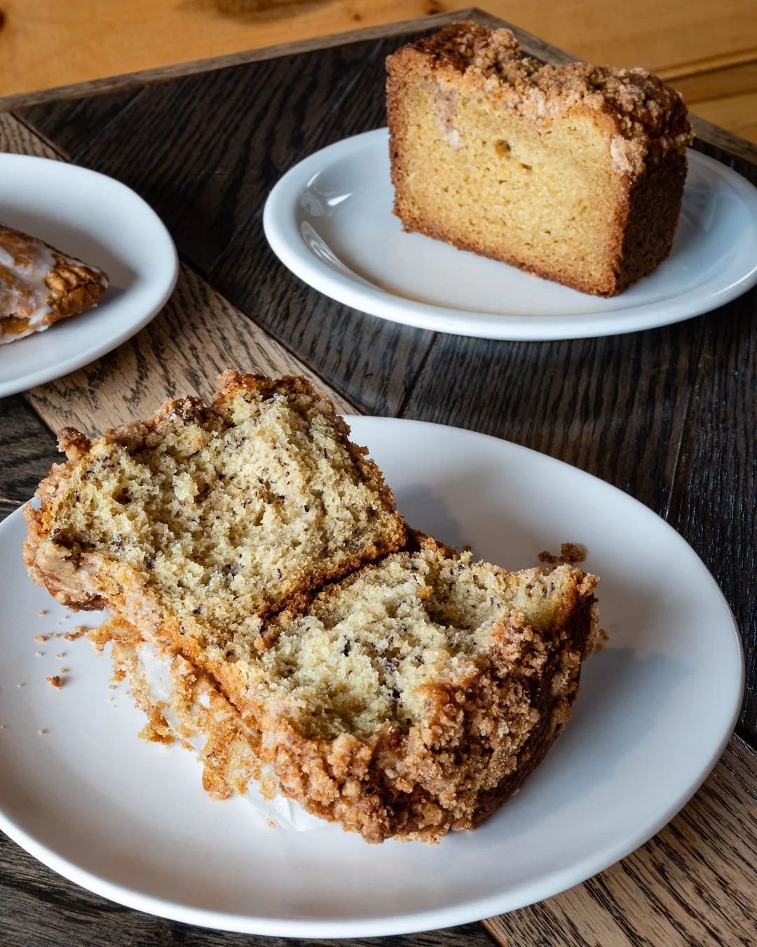 A muffin split in half and a slice of coffee cake on a plate