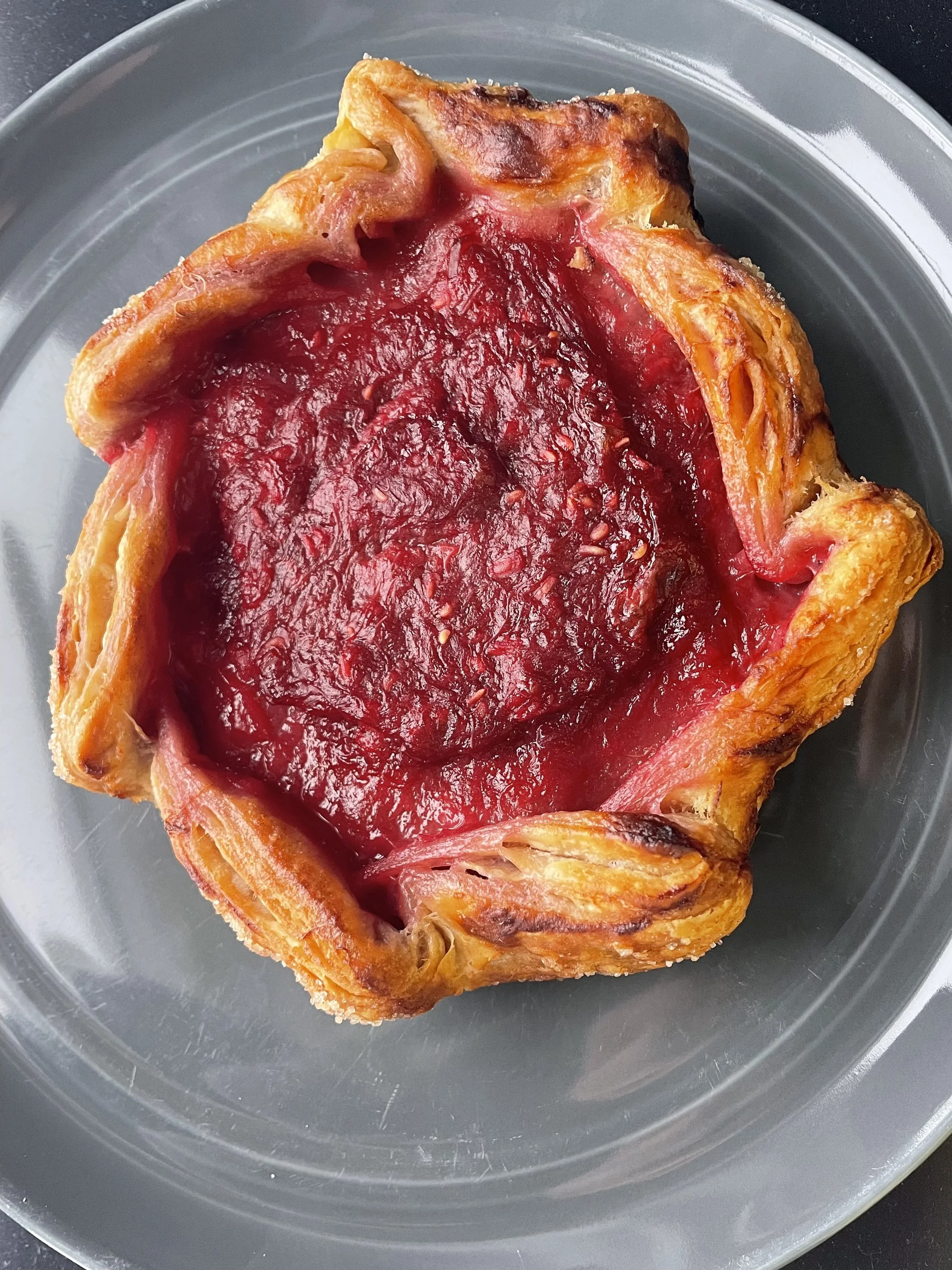 A raspberry tart with a golden crust and a glossy, deep red raspberry filling, placed on a silver dish.