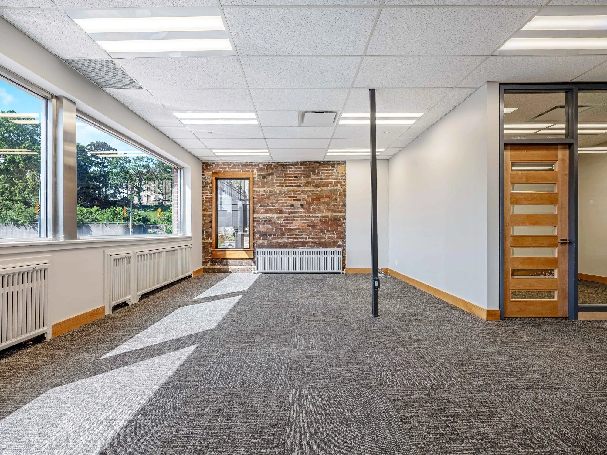 Open office floor with an exposed brick wall, a window and a wood-framed glass door at 8 Macdonell Street, Unit 200A, Guelph
