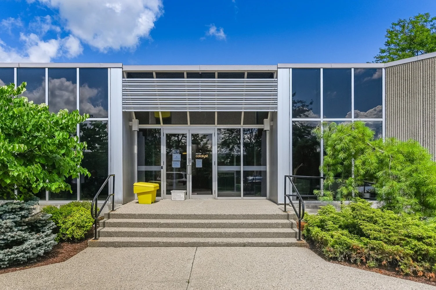 Straight-on view of the 546 Governors Road entrance with glass doors, concrete steps and a yellow salt bin