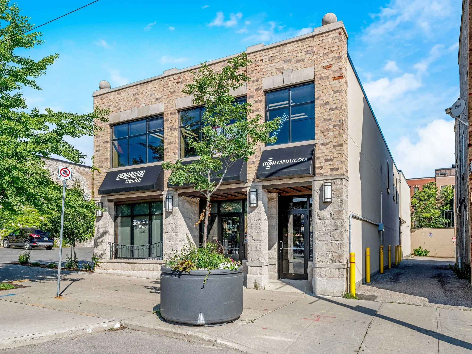 Street view of 18 Macdonell Street, a brick and stone commercial building with a tree and planter at the entrance
