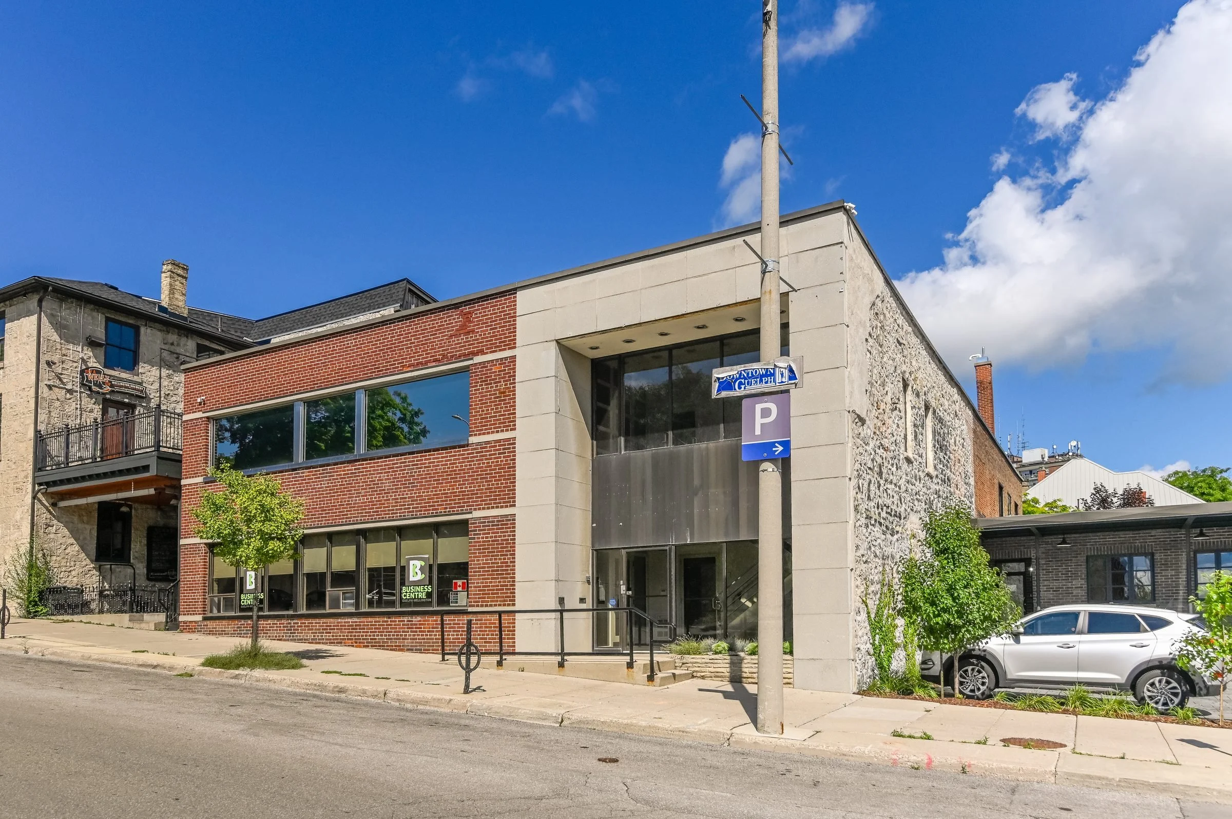 Entrance to the Guelph Mercury Building from the sidewalk, with street signs and a bicycle rack