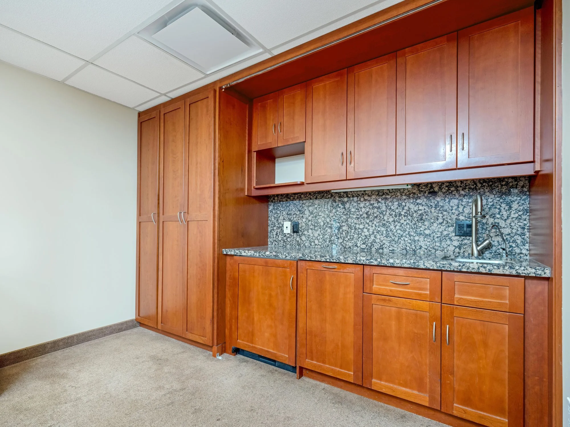 Kitchenette with wood cabinets and granite backsplash