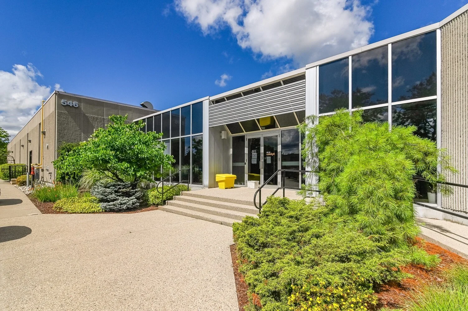 Angled view of the glass entrance at 546 Governors Road with landscaping and a yellow salt bin