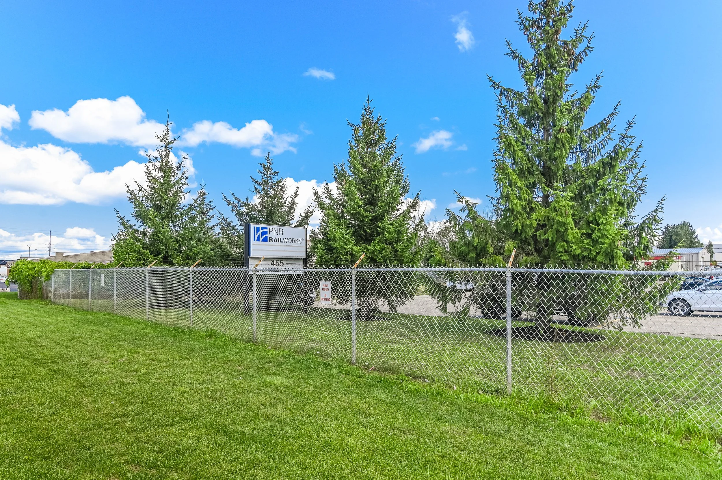 Lawn and chain-link fence lined with evergreen trees at 455 Silvercreek Parkway North