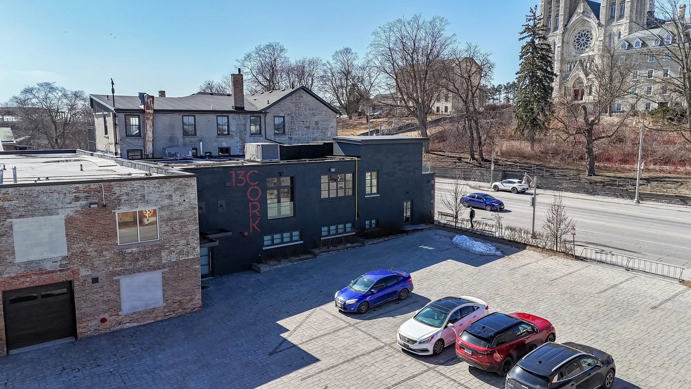 Aerial view of the parking area and dark brick building with the cathedral towers behind, downtown Guelph