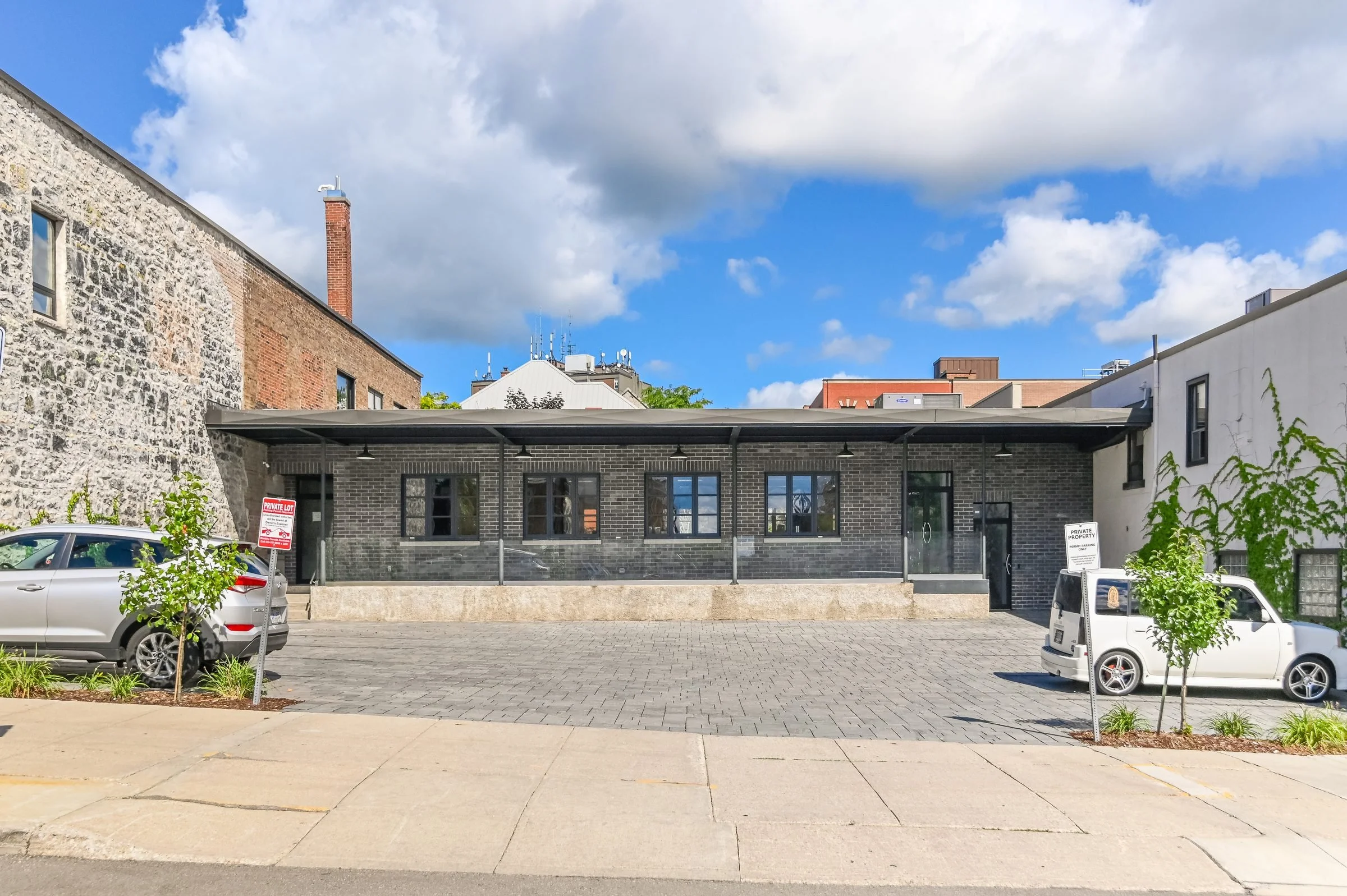 Courtyard side of the Guelph Mercury Building with a stone wall and low dark wing, parking at the front