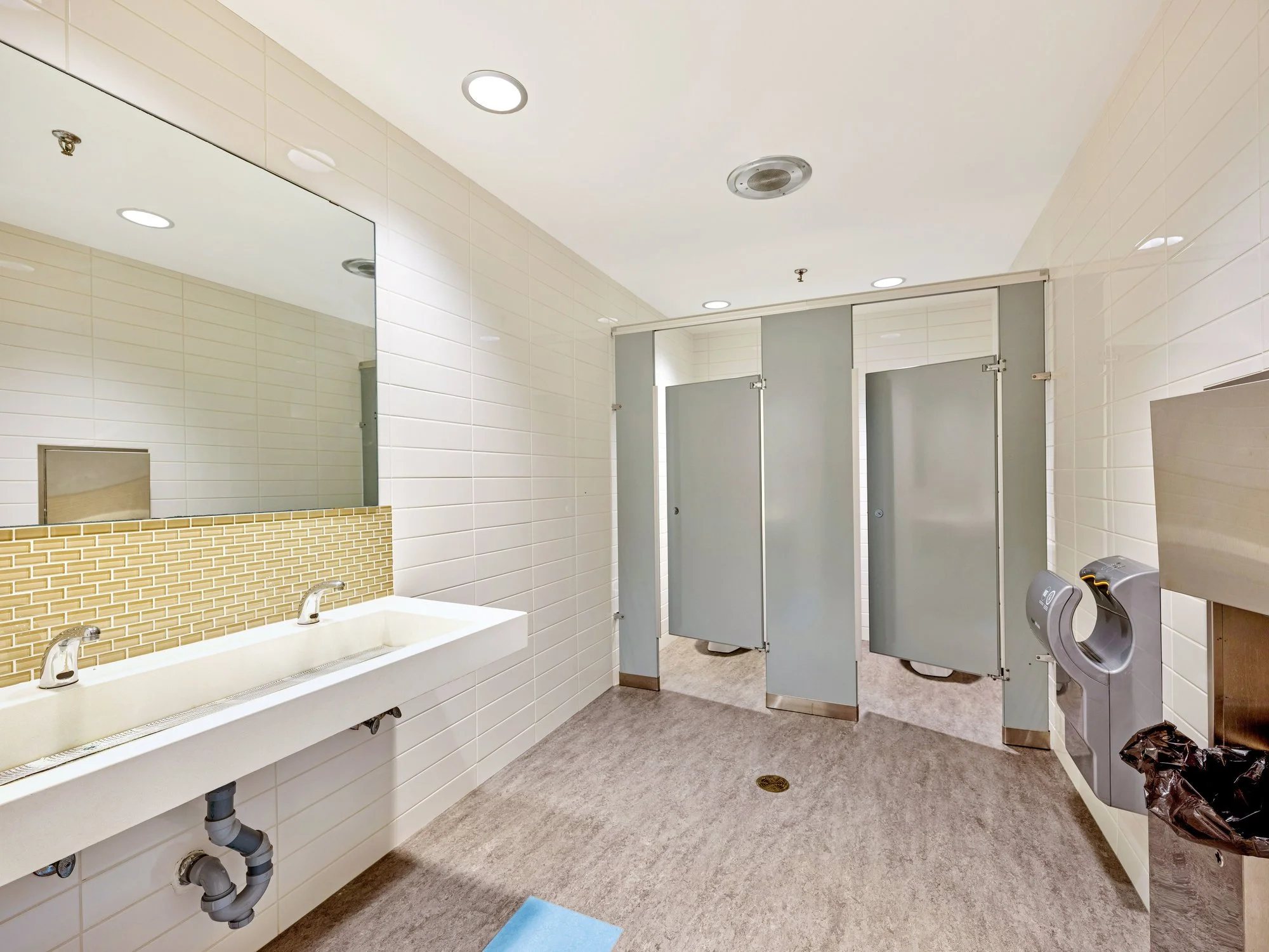 Washroom with a long sink and privacy stalls