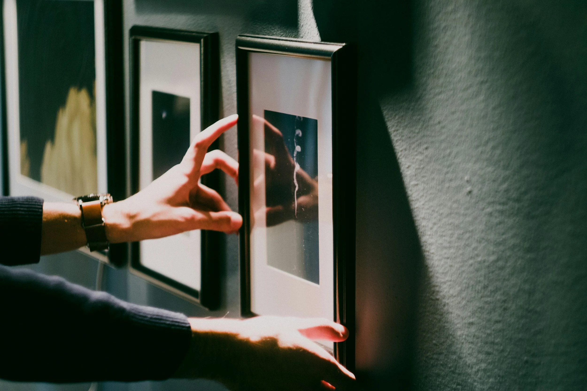 Close-up of a person's hand adjusting photographs in a black picture frame with a blurred background.